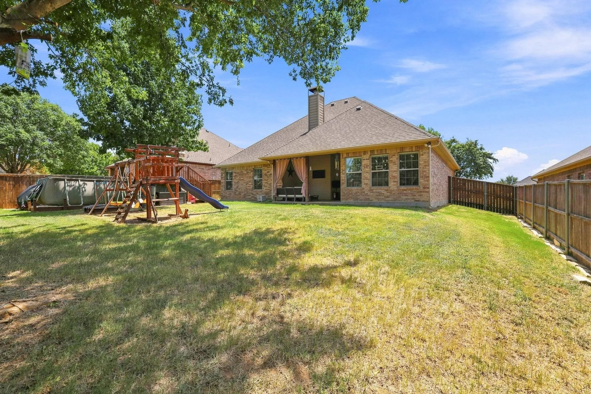 Brick exterior with a covered patio, multiple windows, and a wood privacy fence