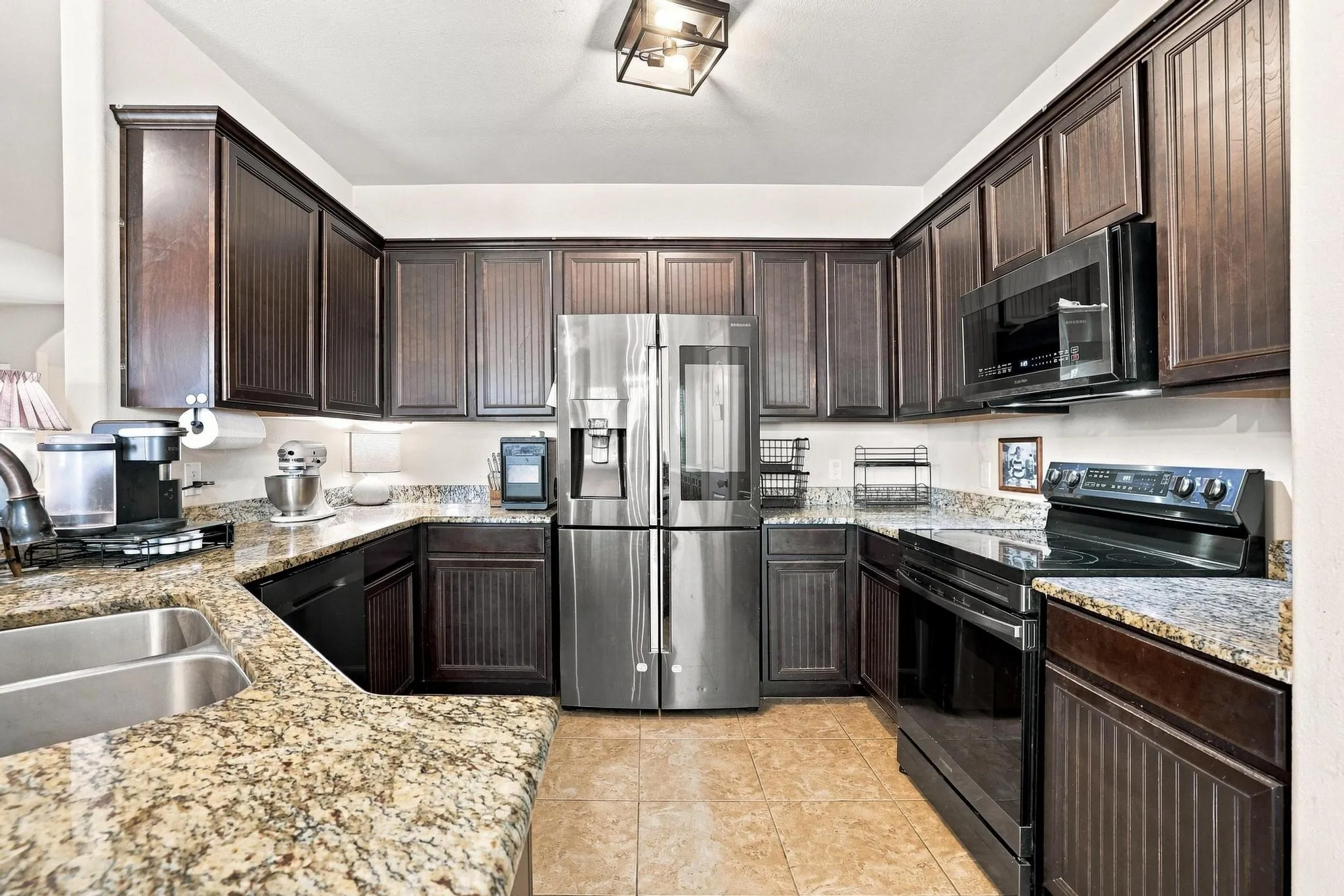 U-shaped kitchen featuring dark wood cabinetry, granite countertops, tile flooring, and stainless steel appliances