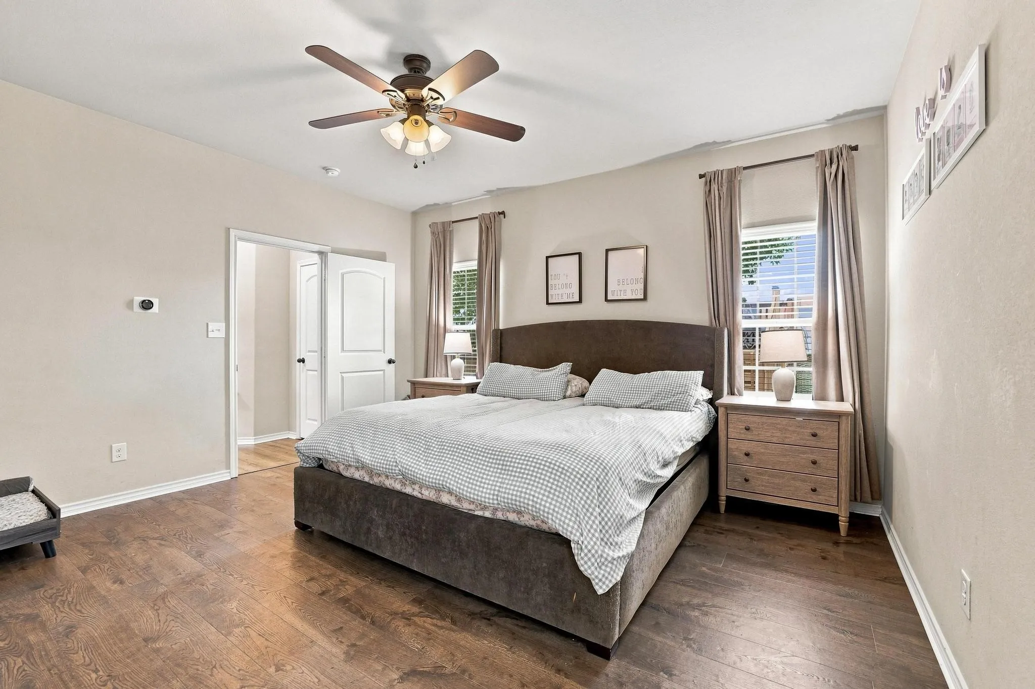Spacious room featuring wood-finish flooring, a ceiling fan with integrated lighting, and two windows with blinds