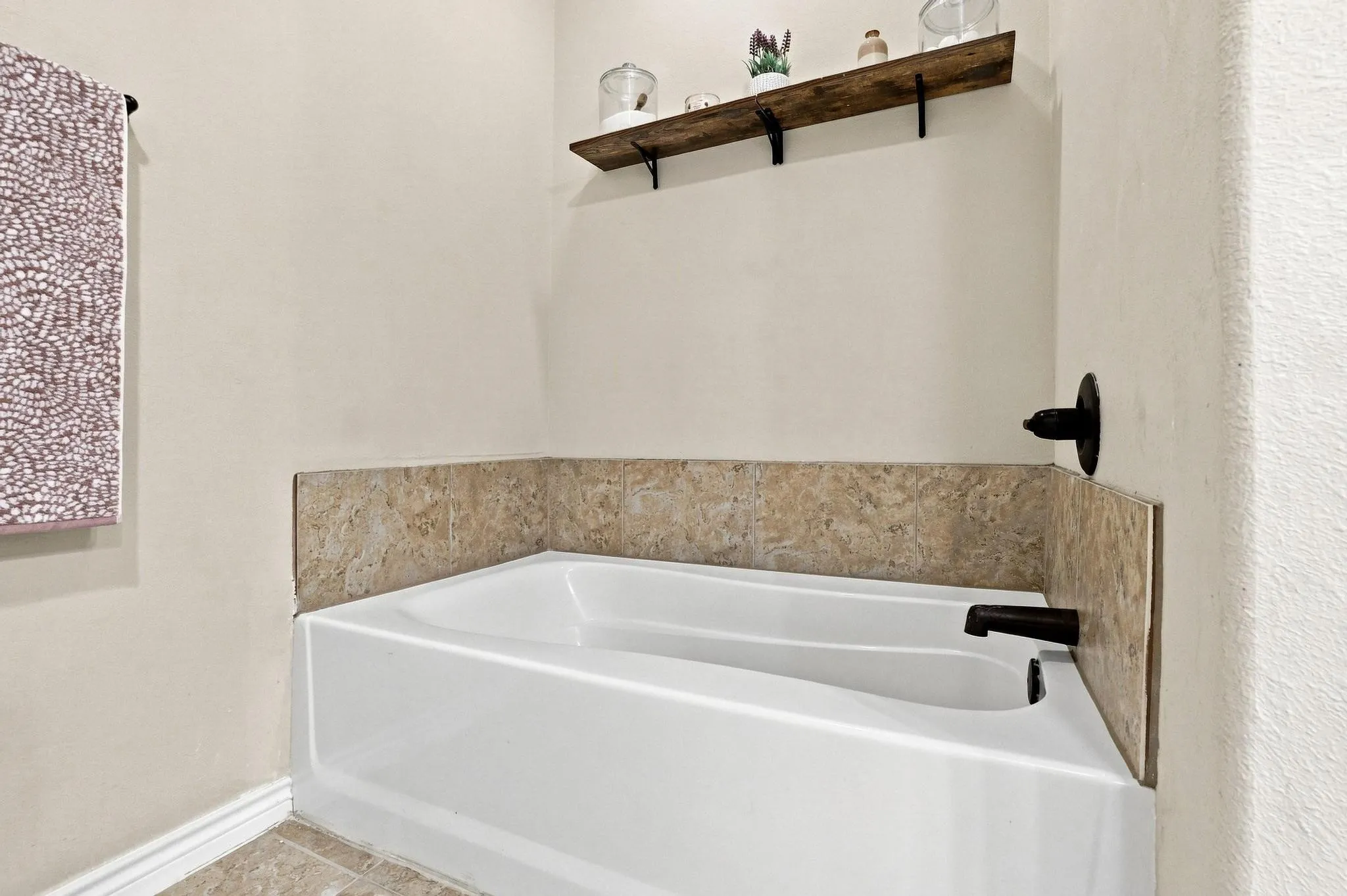 White bathtub with a tiled surround, featuring a dark bronze faucet and a decorative wall shelf