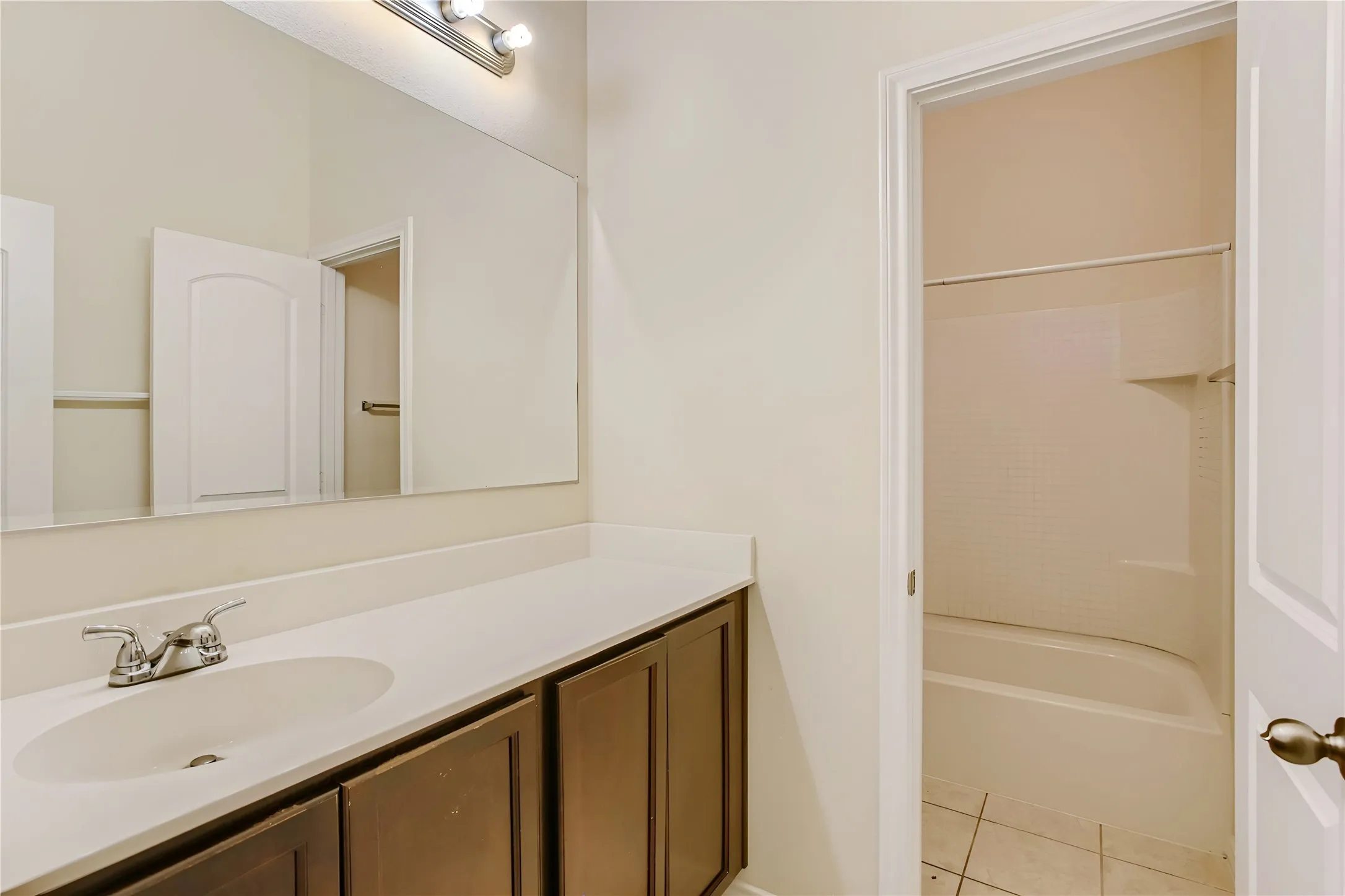 Vanity with a white countertop and dark wood-finish cabinetry, a large mirror, and a built-in bathtub with a shower kit