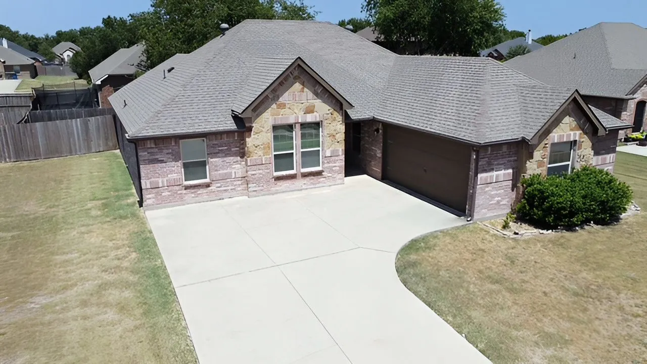Brick and stone exterior with a shingle roof, attached garage, and a concrete driveway