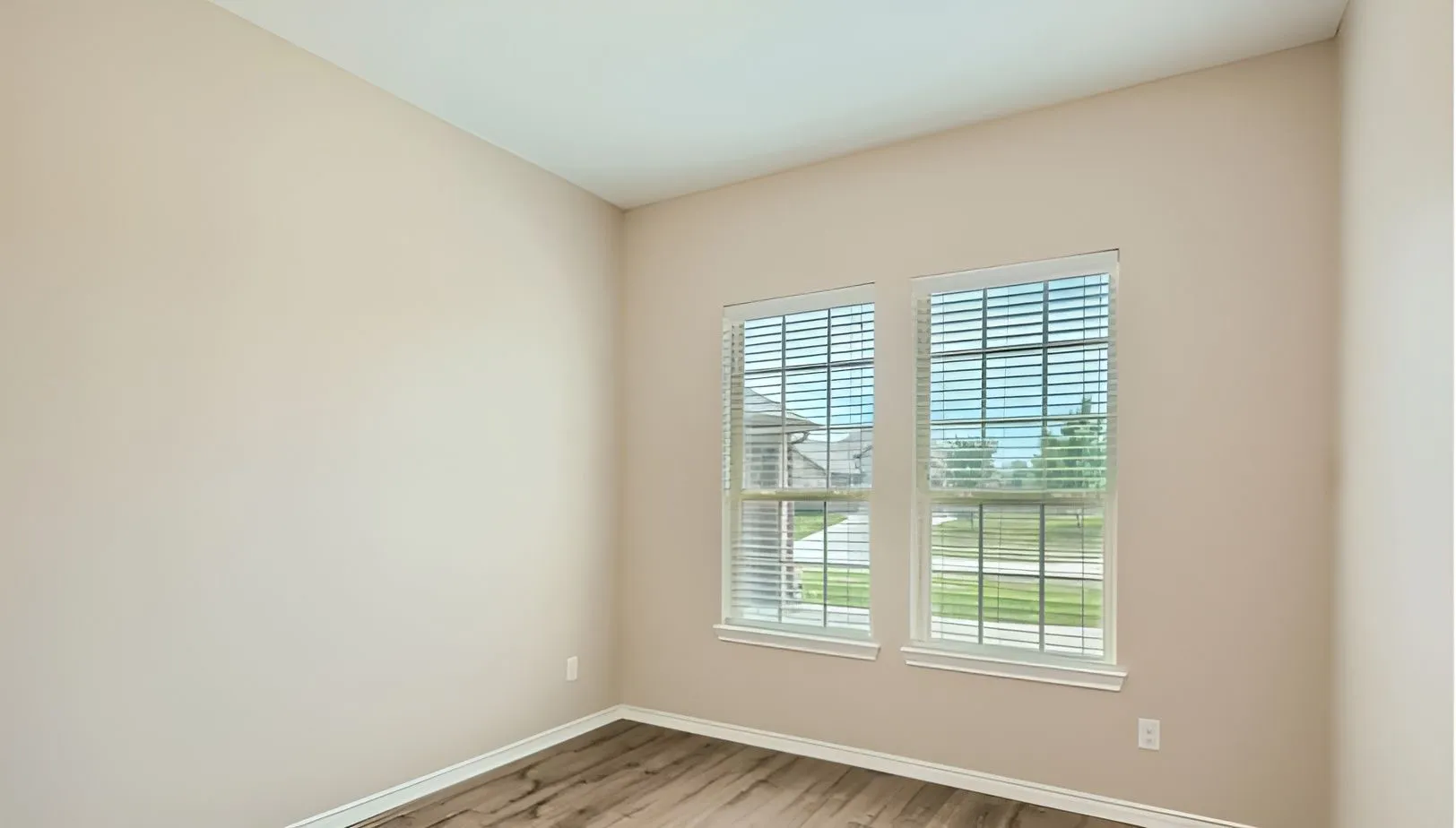 Warm neutral wall color, wood-finish flooring, and two windows with blinds