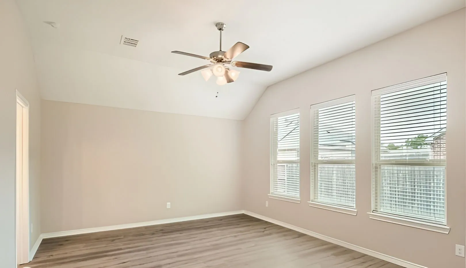 Vaulted ceiling with a ceiling fan, three windows with blinds, and wood-finish flooring