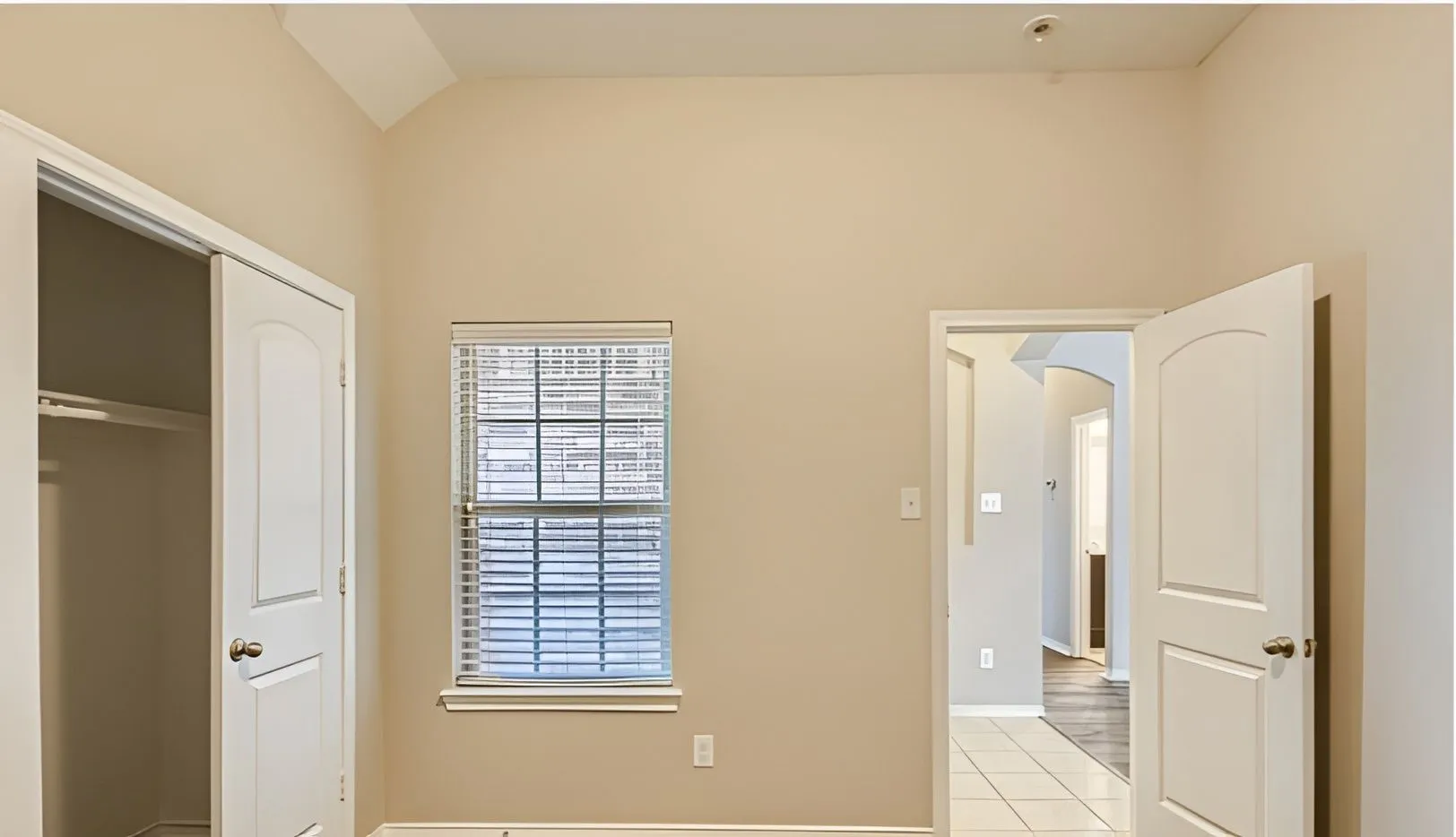 Vaulted ceiling, arched doorway, window with blinds, tile flooring, and closet space with bi-fold doors
