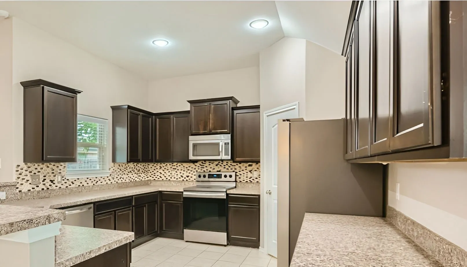 Kitchen featuring dark wood-finish cabinetry, light speckled countertops, a patterned tile backsplash, stainless steel appliances, and recessed lighting