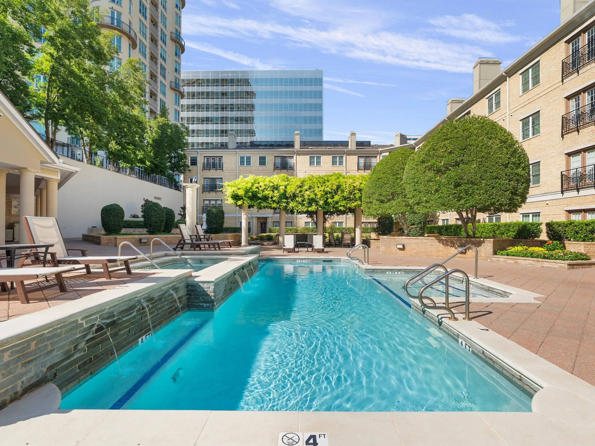 Outdoor swimming pool featuring integrated spa, surrounding paver patio, lush landscaping, and built-in planters