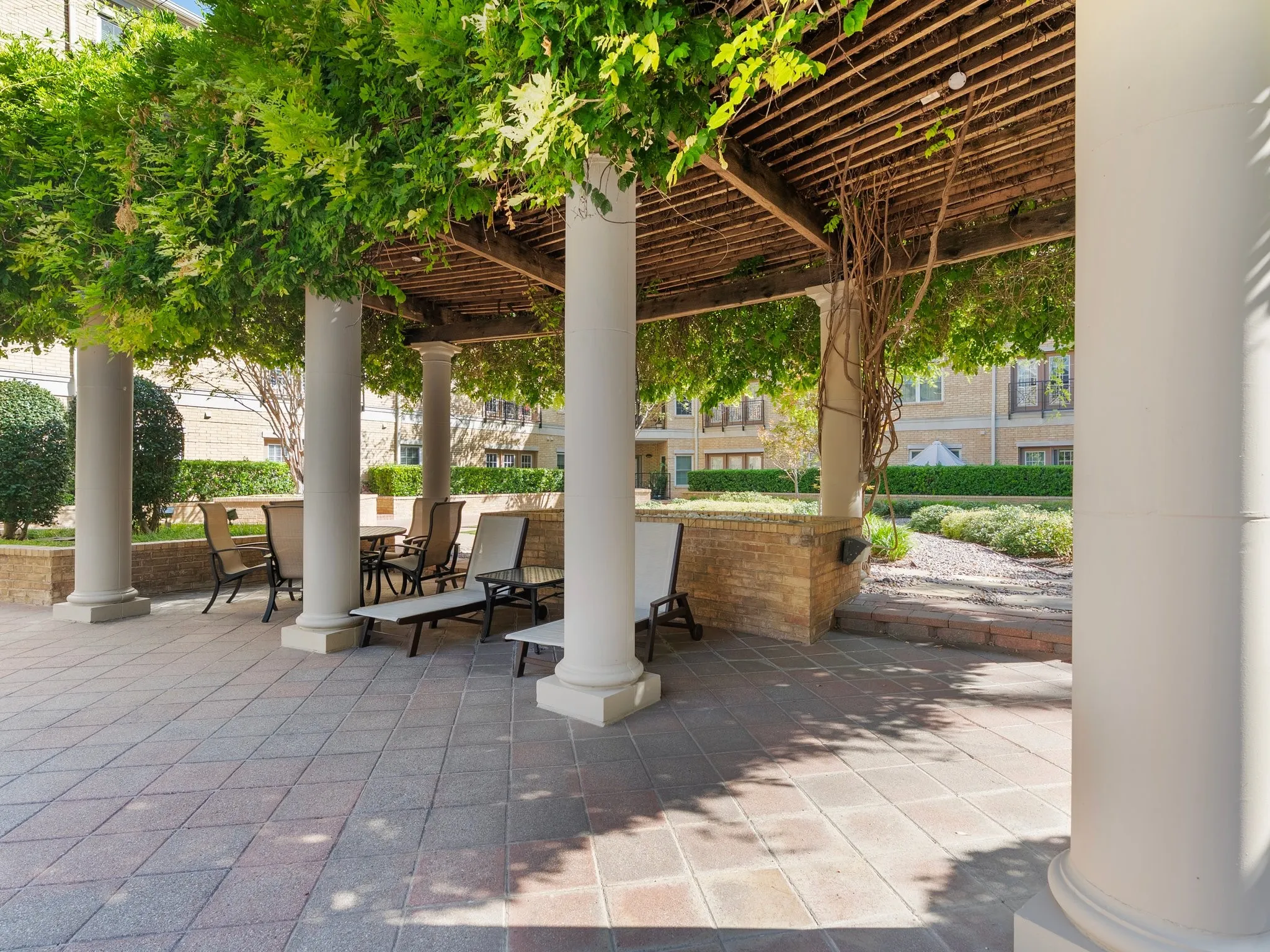 Tiled outdoor patio with a pergola, supporting columns, and a brick retaining wall