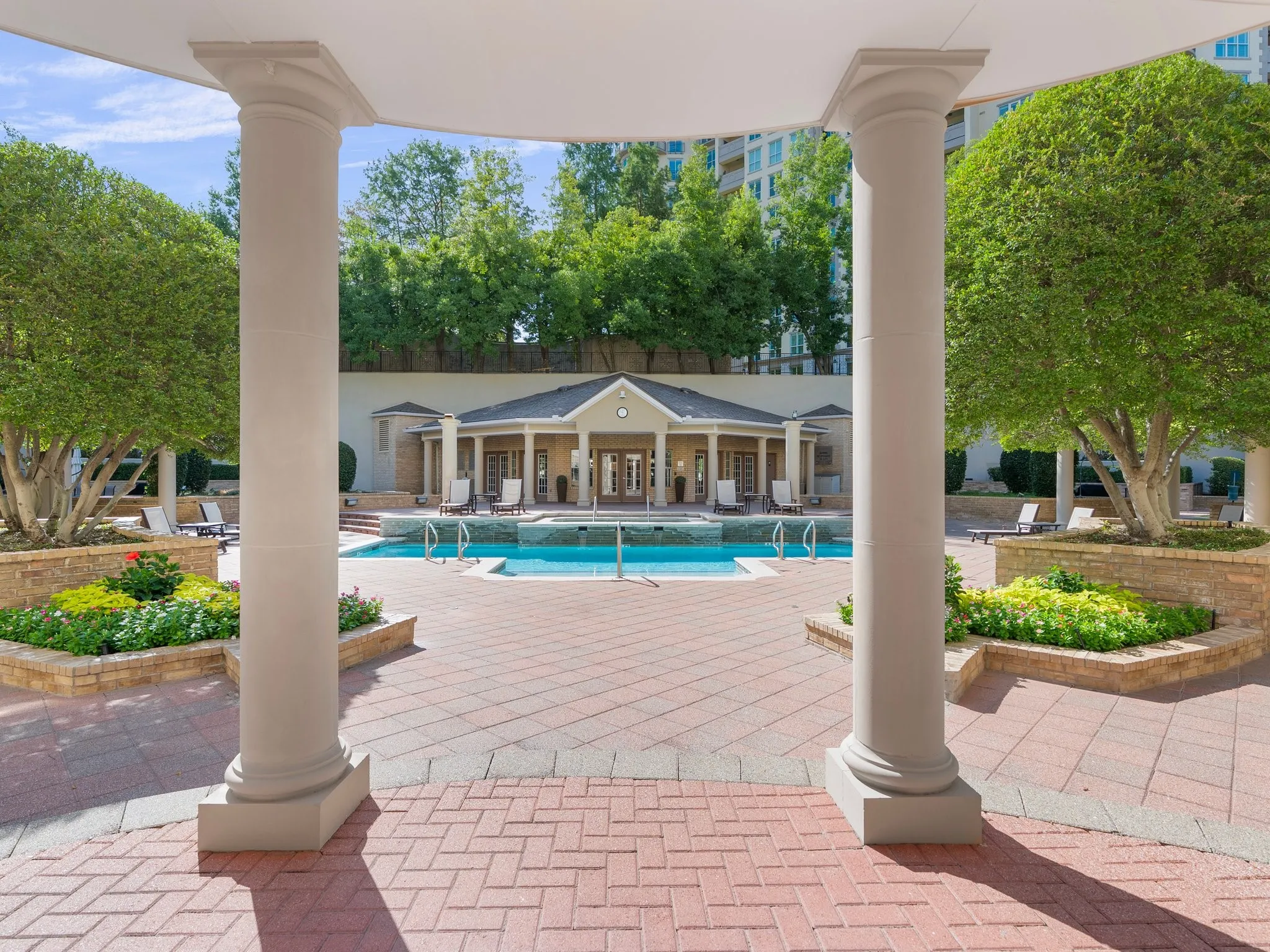 Expansive paver patio with a central swimming pool and surrounding green landscaping