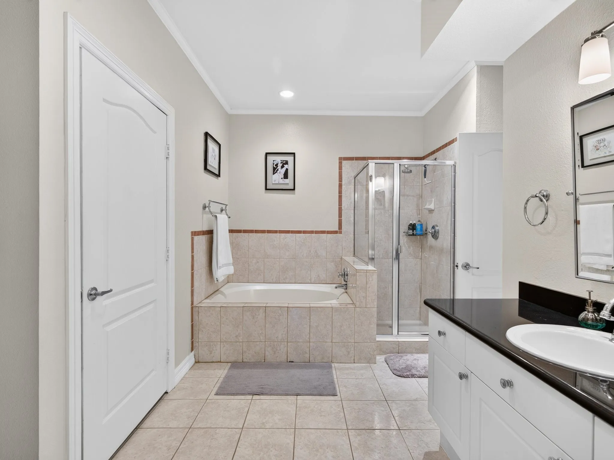 Built-in soaking tub, glass-enclosed shower, dual-door vanity with dark countertop, and tiled flooring
