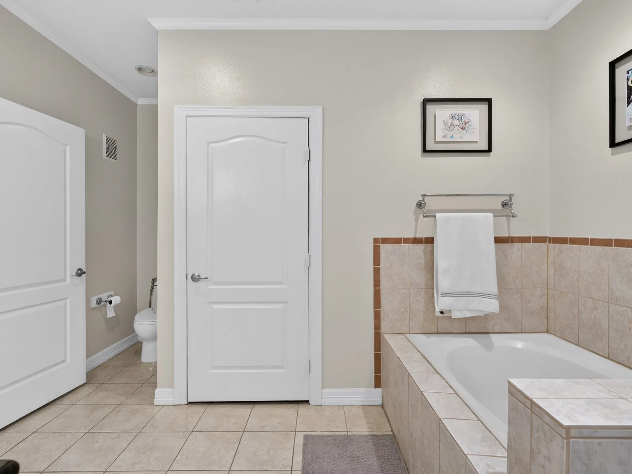 Built-in soaking tub with tile surround, neutral-toned wall paint, white trim, and tile flooring