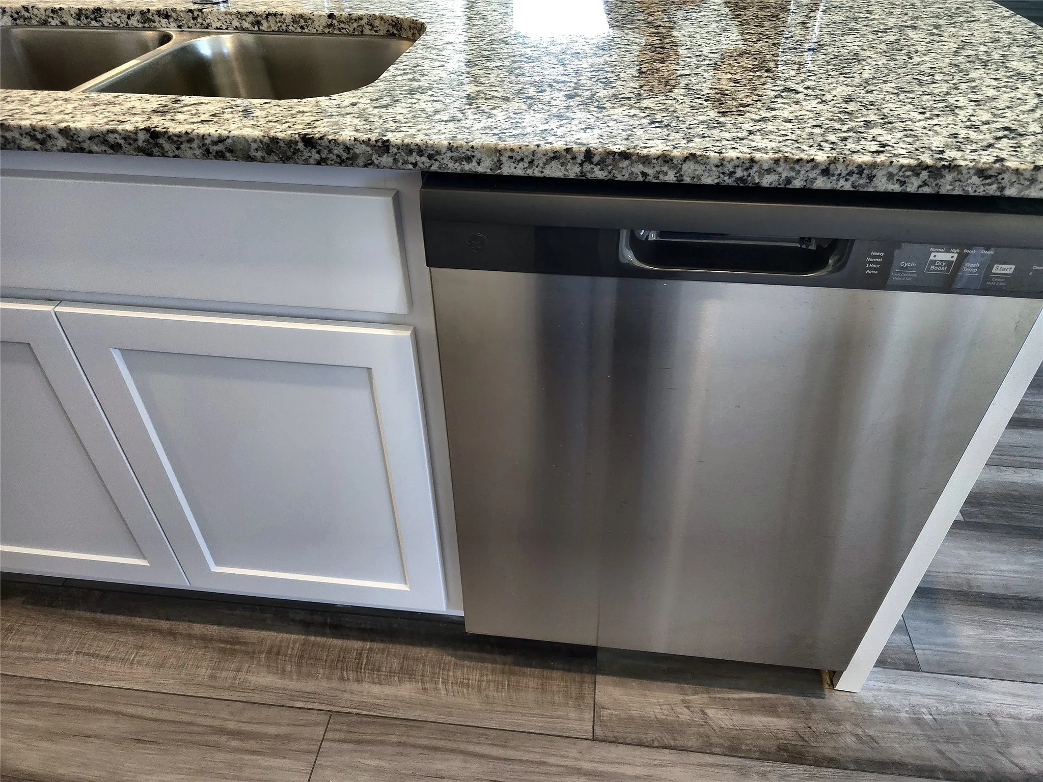 Stainless steel double basin sink, granite-style countertop, white shaker-style cabinetry, and stainless steel dishwasher