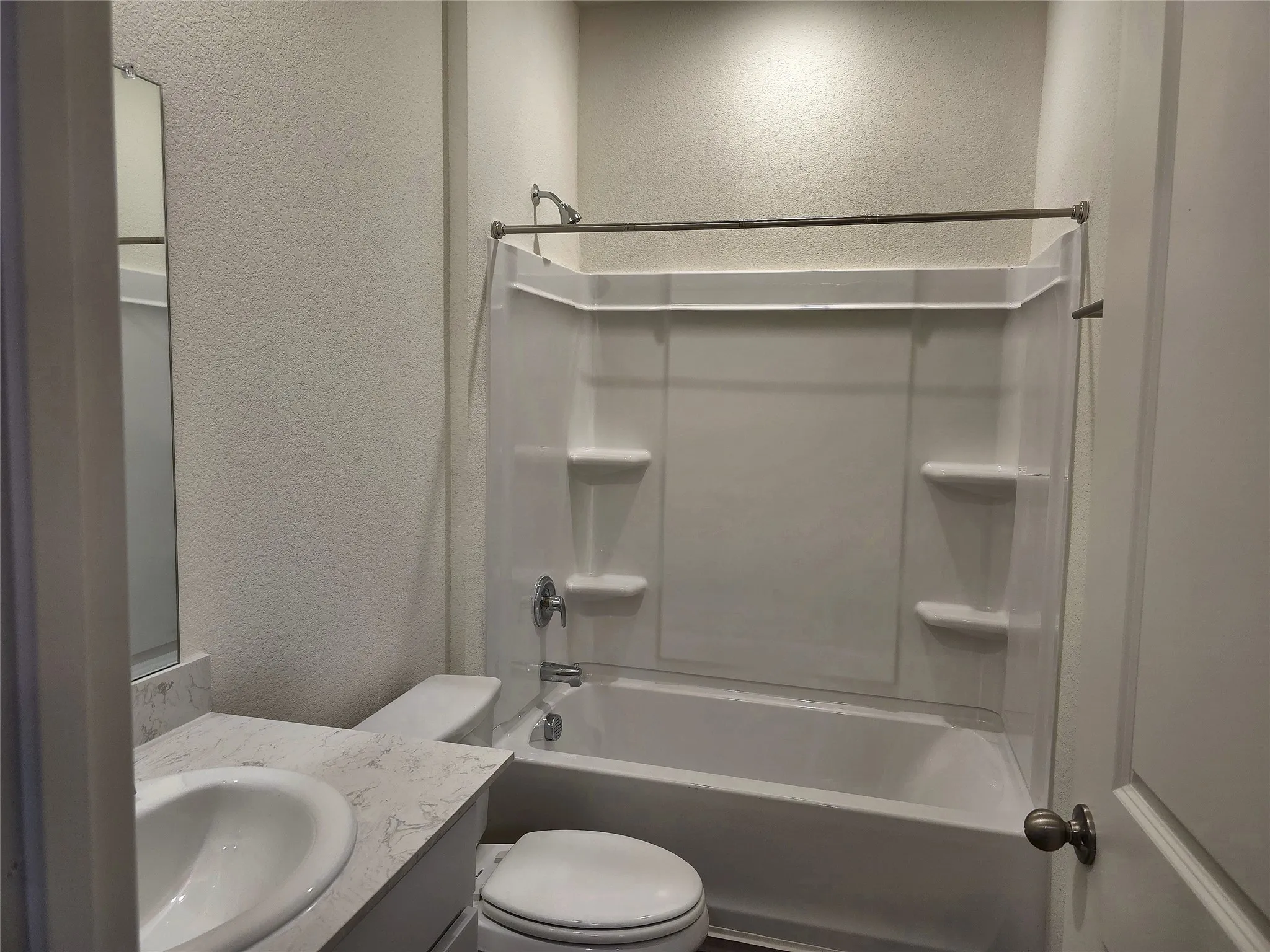 White tub and shower combination with chrome fixtures, integrated shelving, and a curved shower rod