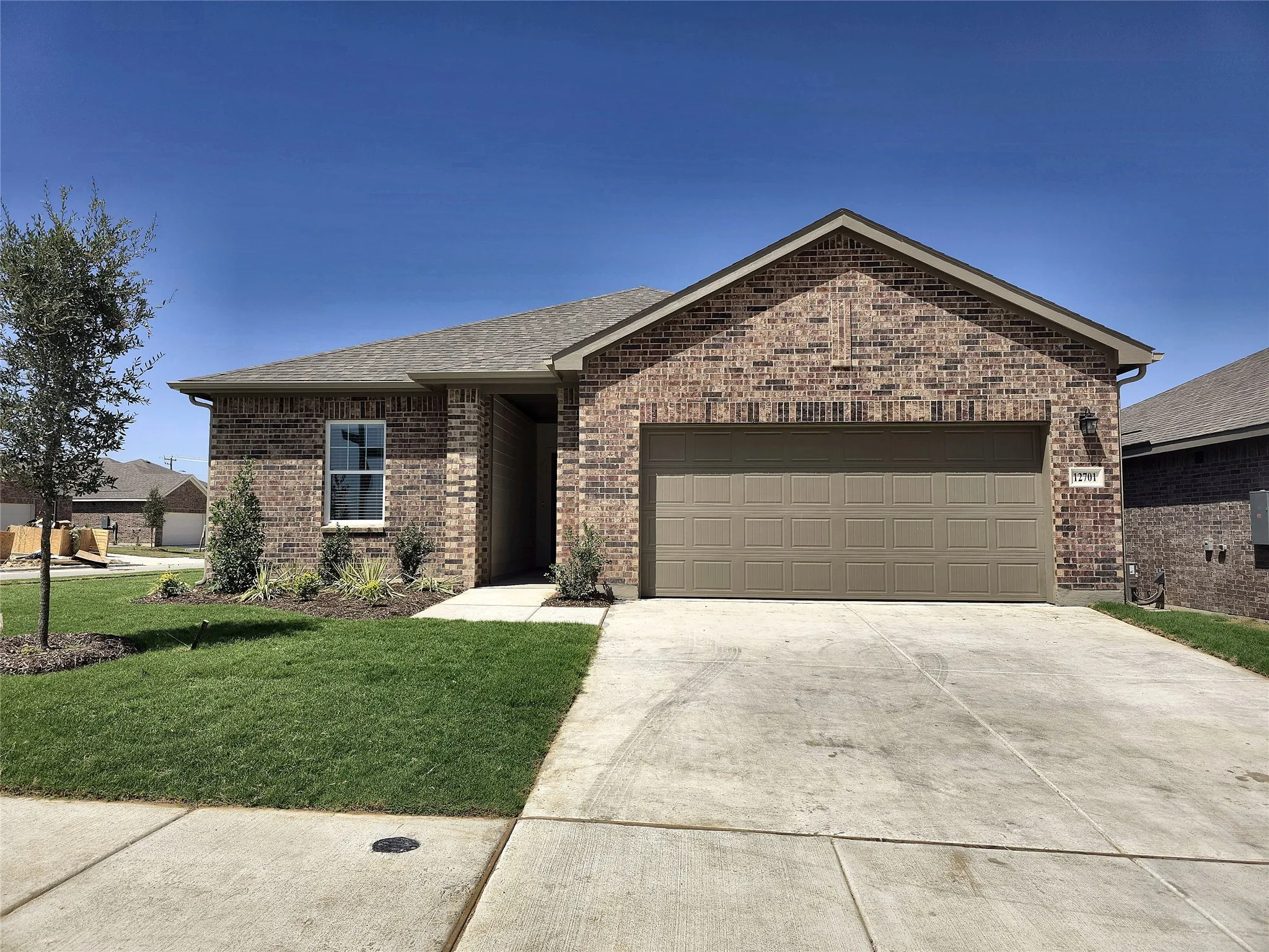 Brick exterior with a gabled roofline, an attached garage, a concrete driveway, and established landscaping