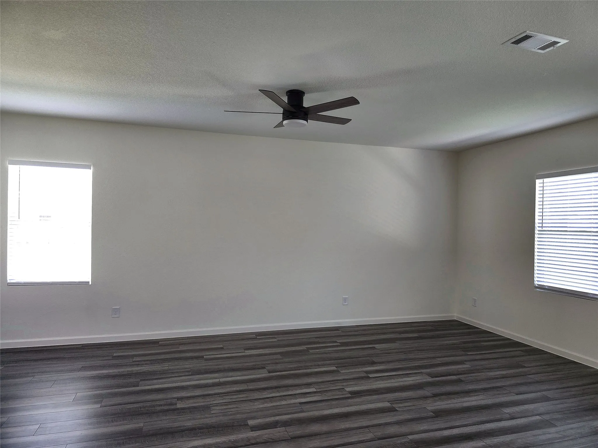 Spacious room featuring wood-finish flooring, white walls, and a ceiling fan