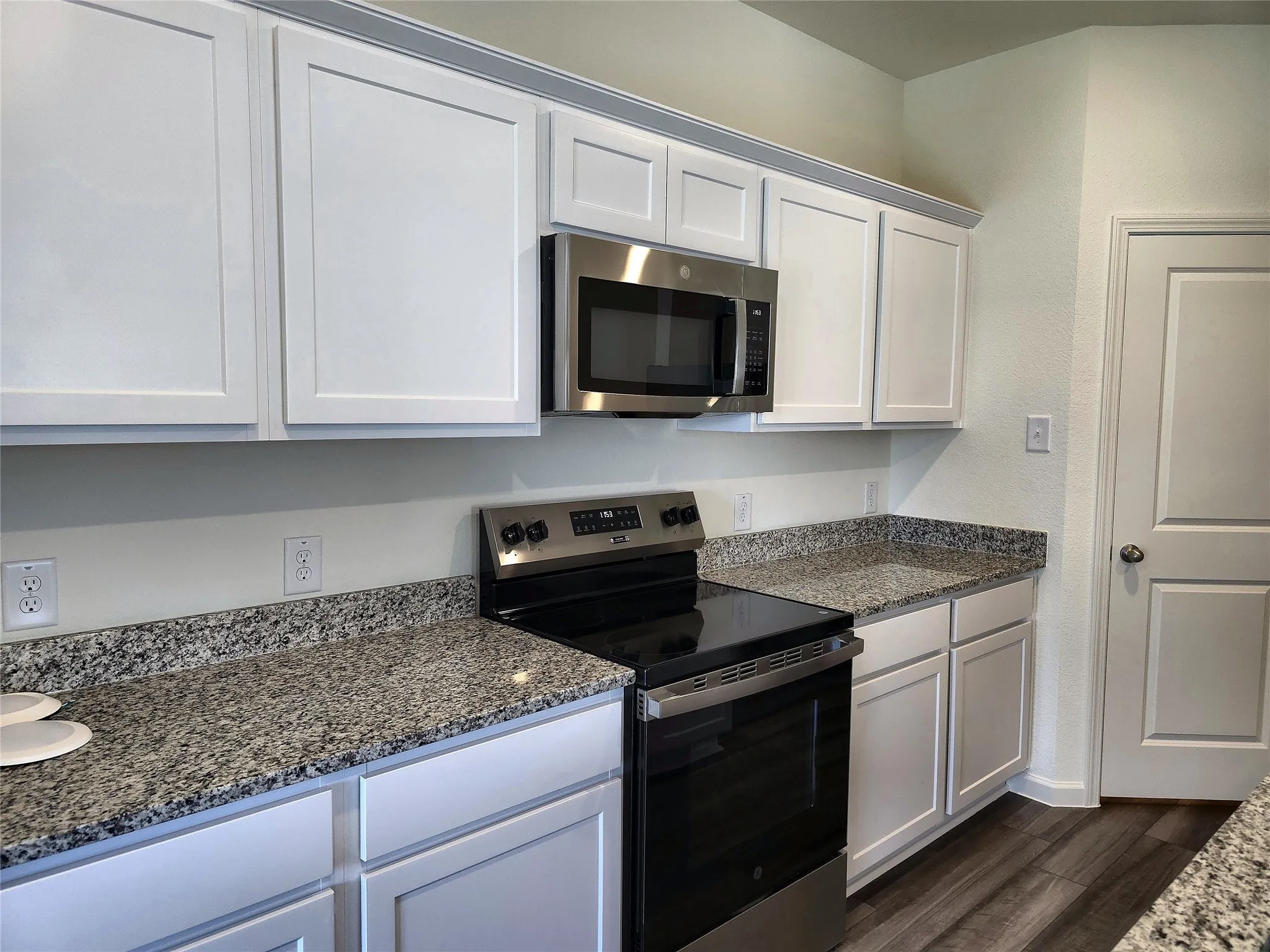 White shaker-style cabinetry with crown molding, stainless steel microwave, black electric range, and speckled countertops