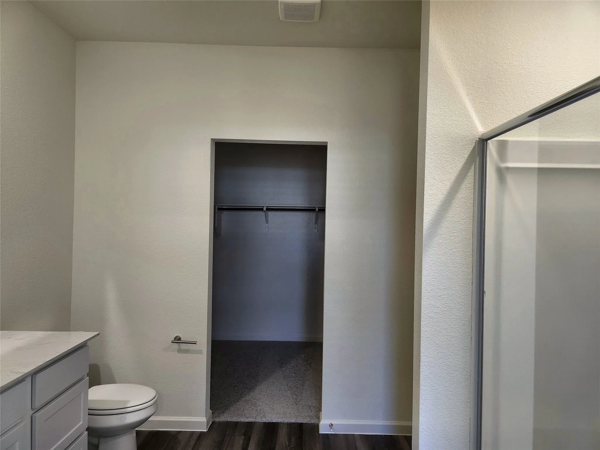 Bathroom with a white toilet, light gray vanity with a light-colored countertop, and a shower enclosure with a clear glass panel