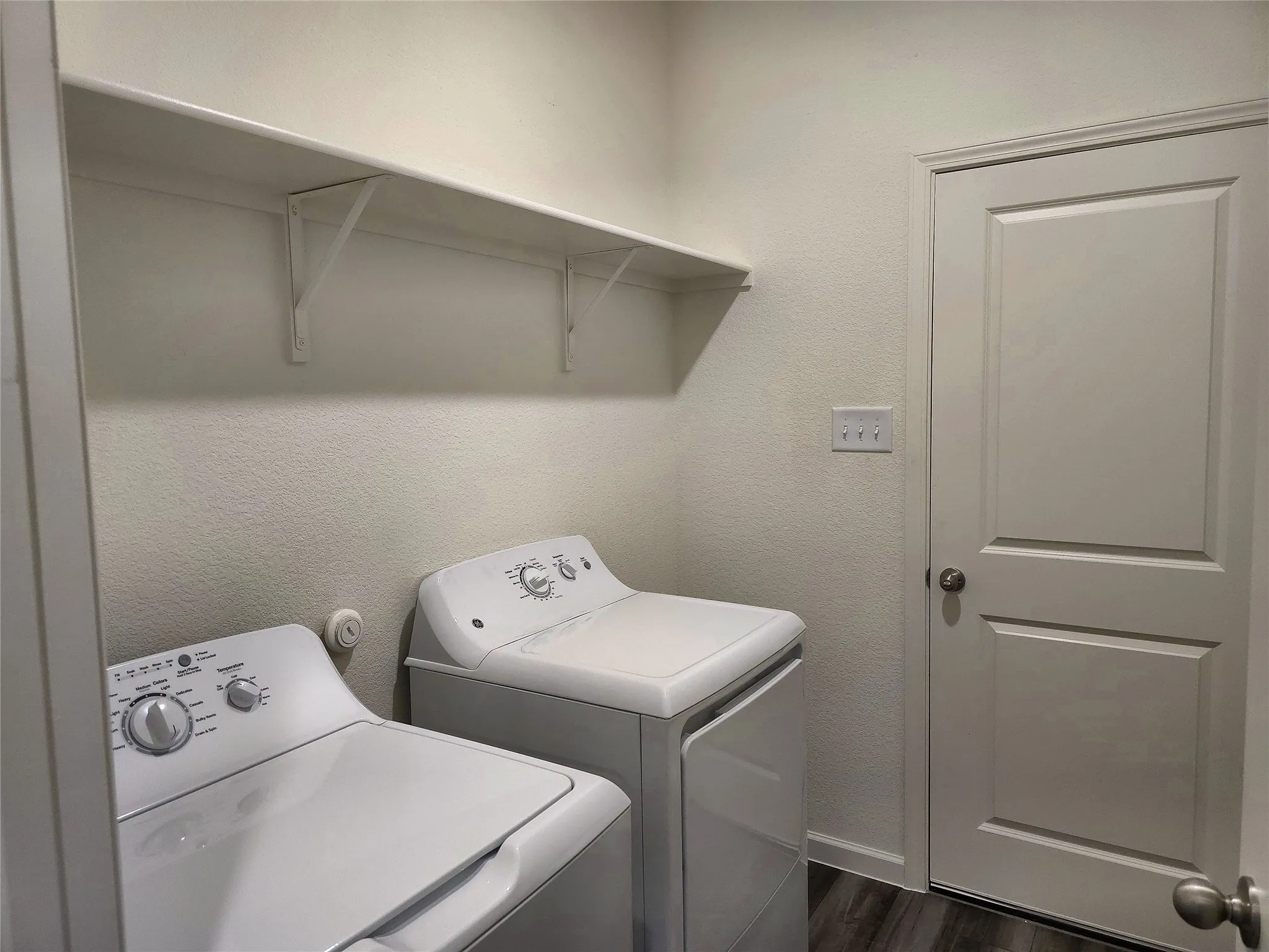White walls with textured finish, overhead shelving, paneled door, and wood-finish flooring