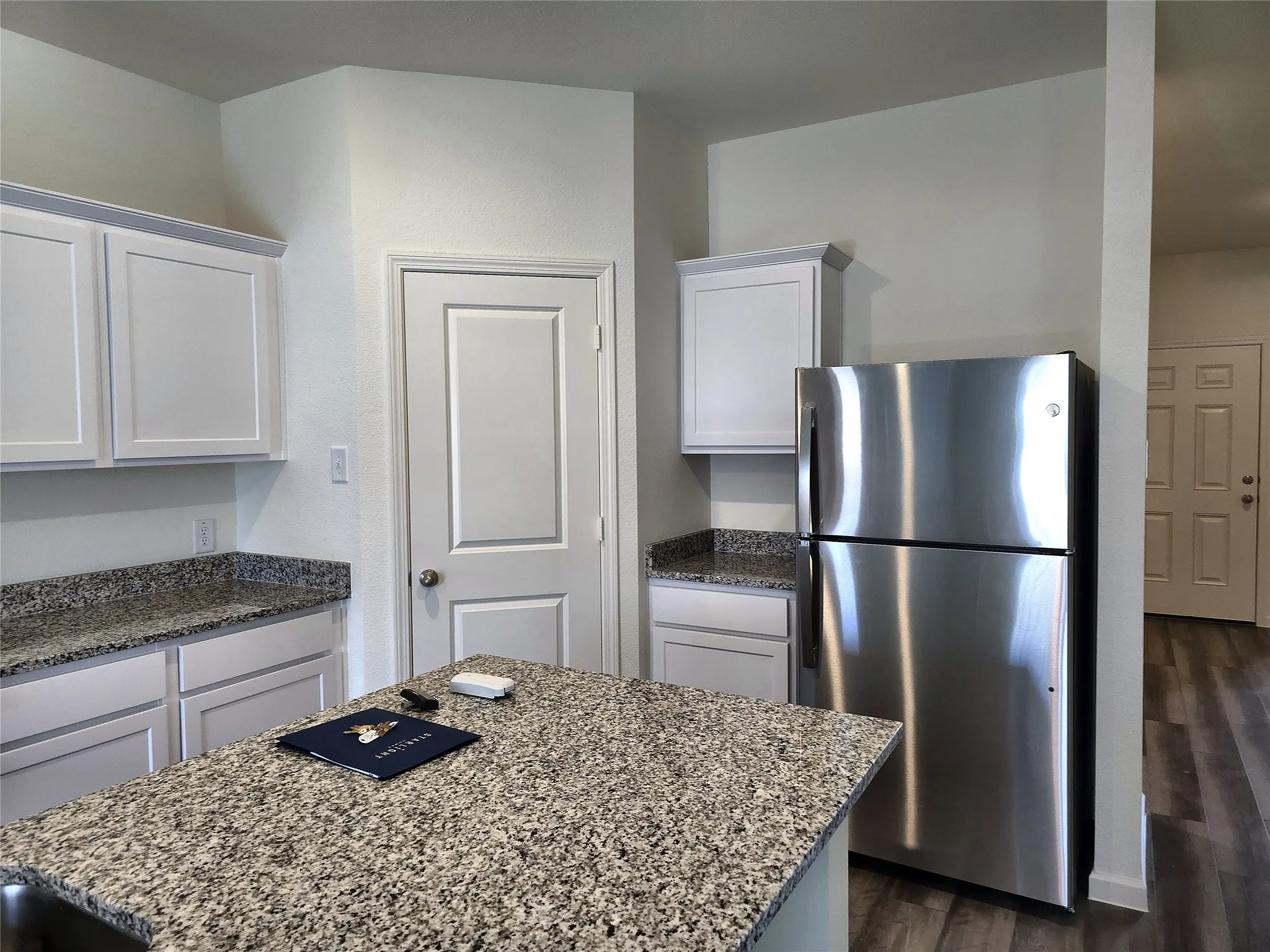 Kitchen featuring white shaker-style cabinetry, granite countertops, stainless steel refrigerator, and wood-finish flooring