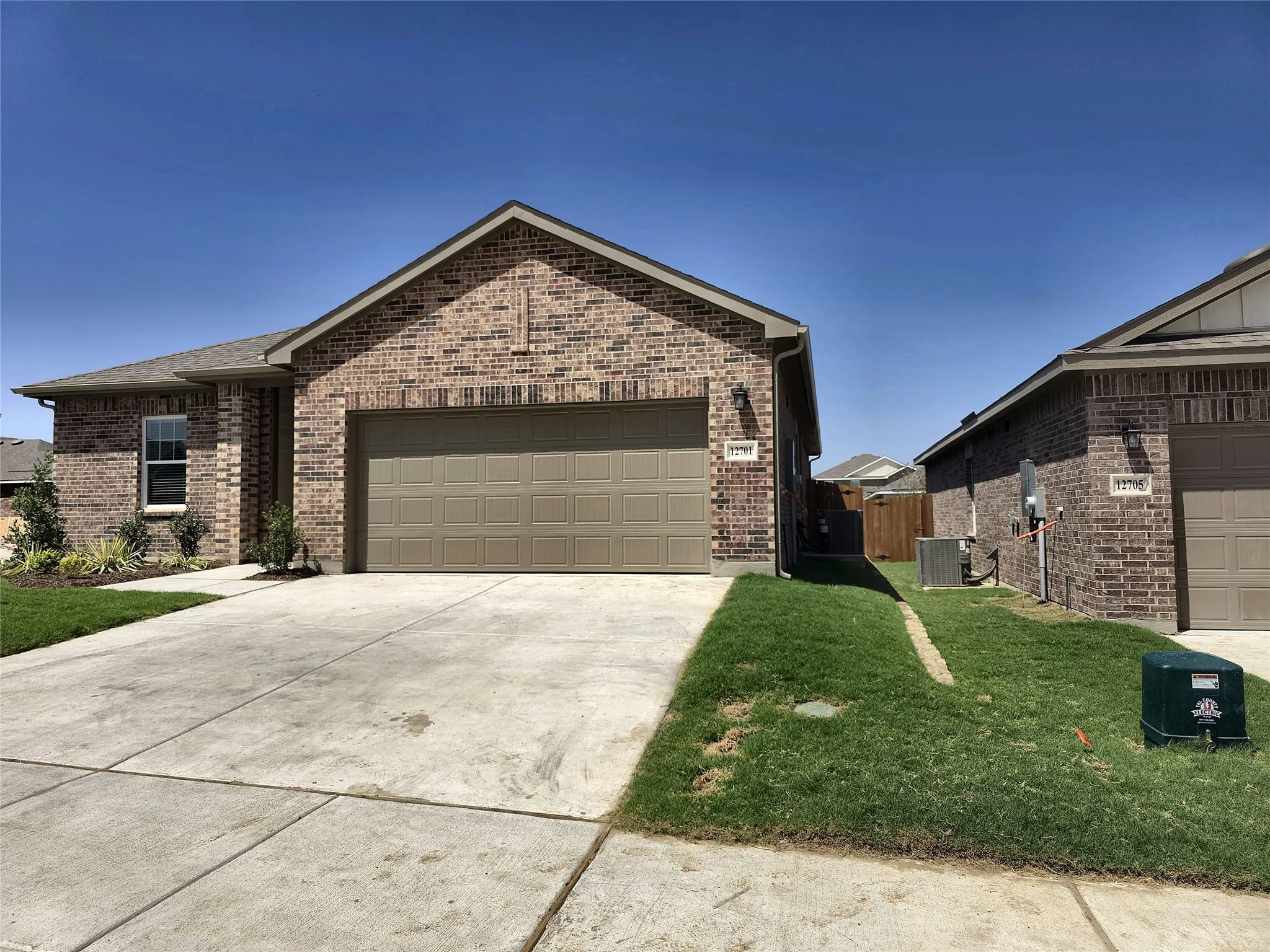 Brick exterior, attached garage, concrete driveway, front landscaping, and a pitched roof