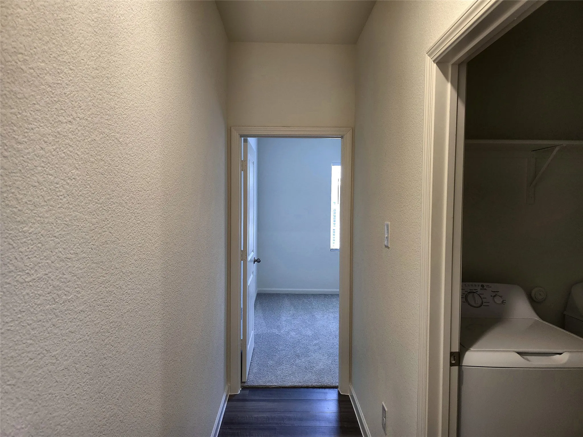 Hallway featuring wood-finish flooring, textured walls, and a laundry closet with shelving