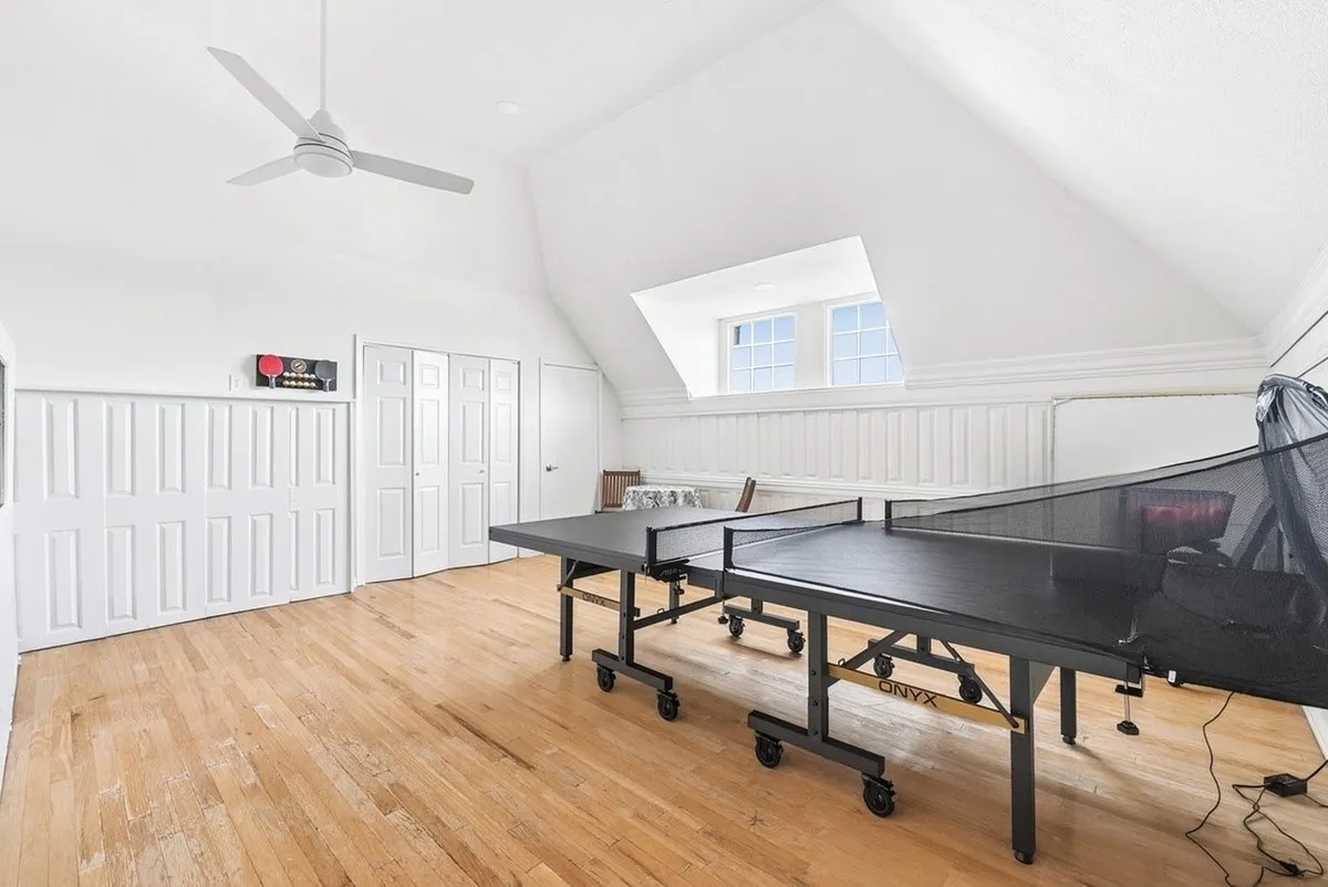 Sloped ceiling room featuring wood-finish flooring, a ceiling fan, white paneled walls, and built-in closet doors