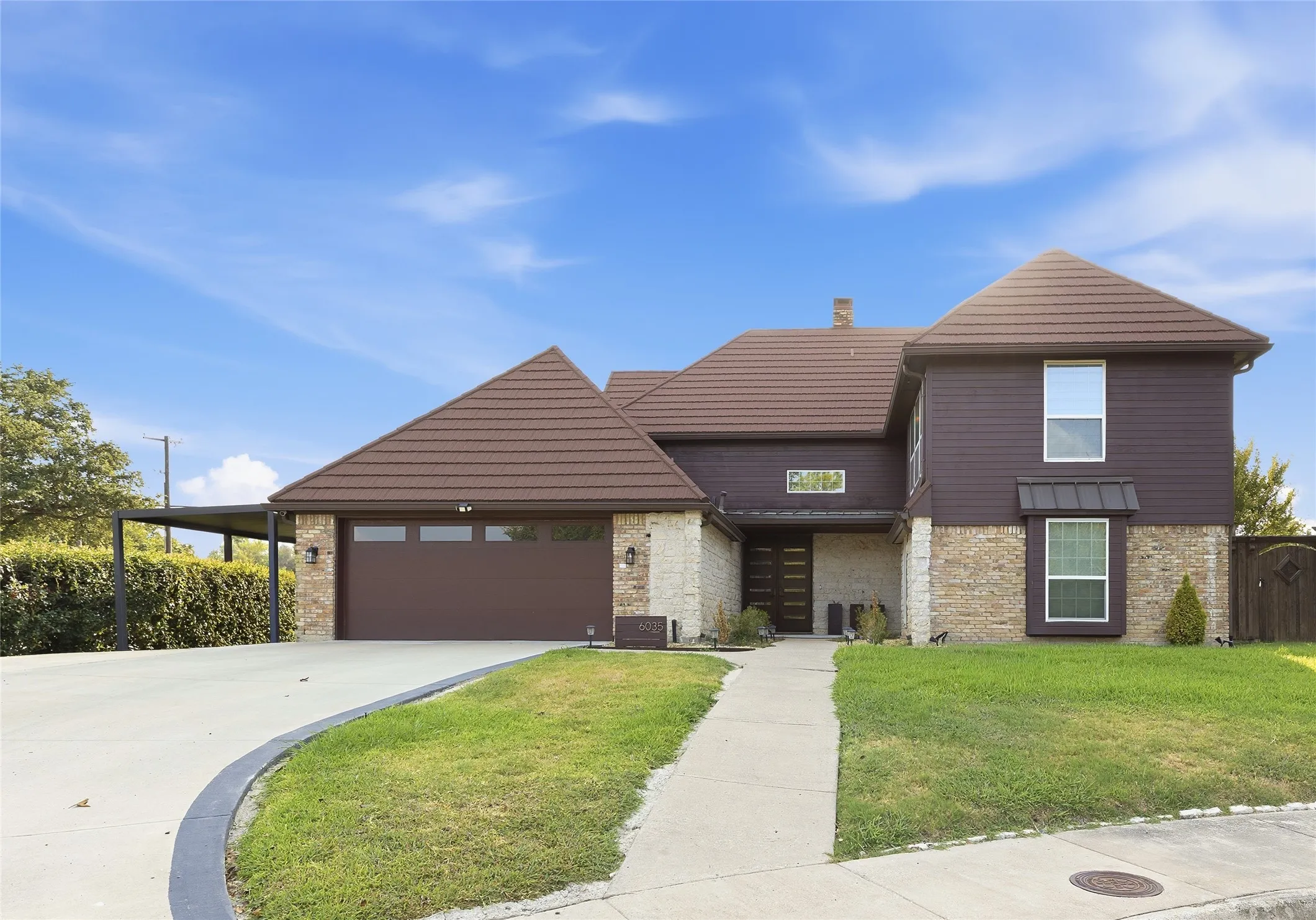 Stone and siding exterior with a multi-level tile roof, featuring an attached two-car garage, covered carport, and a concrete driveway