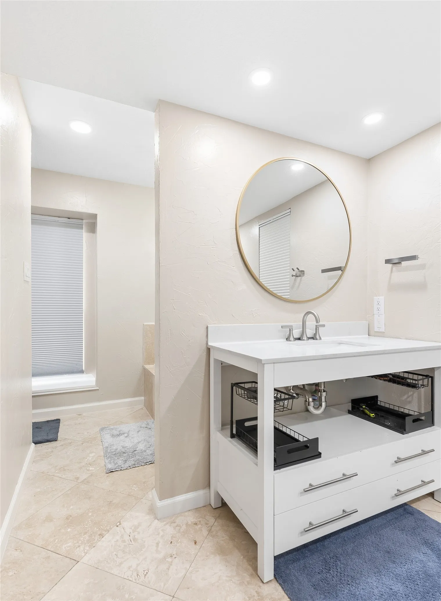 White vanity with undermount sink, circular mirror, recessed lighting, and tile flooring