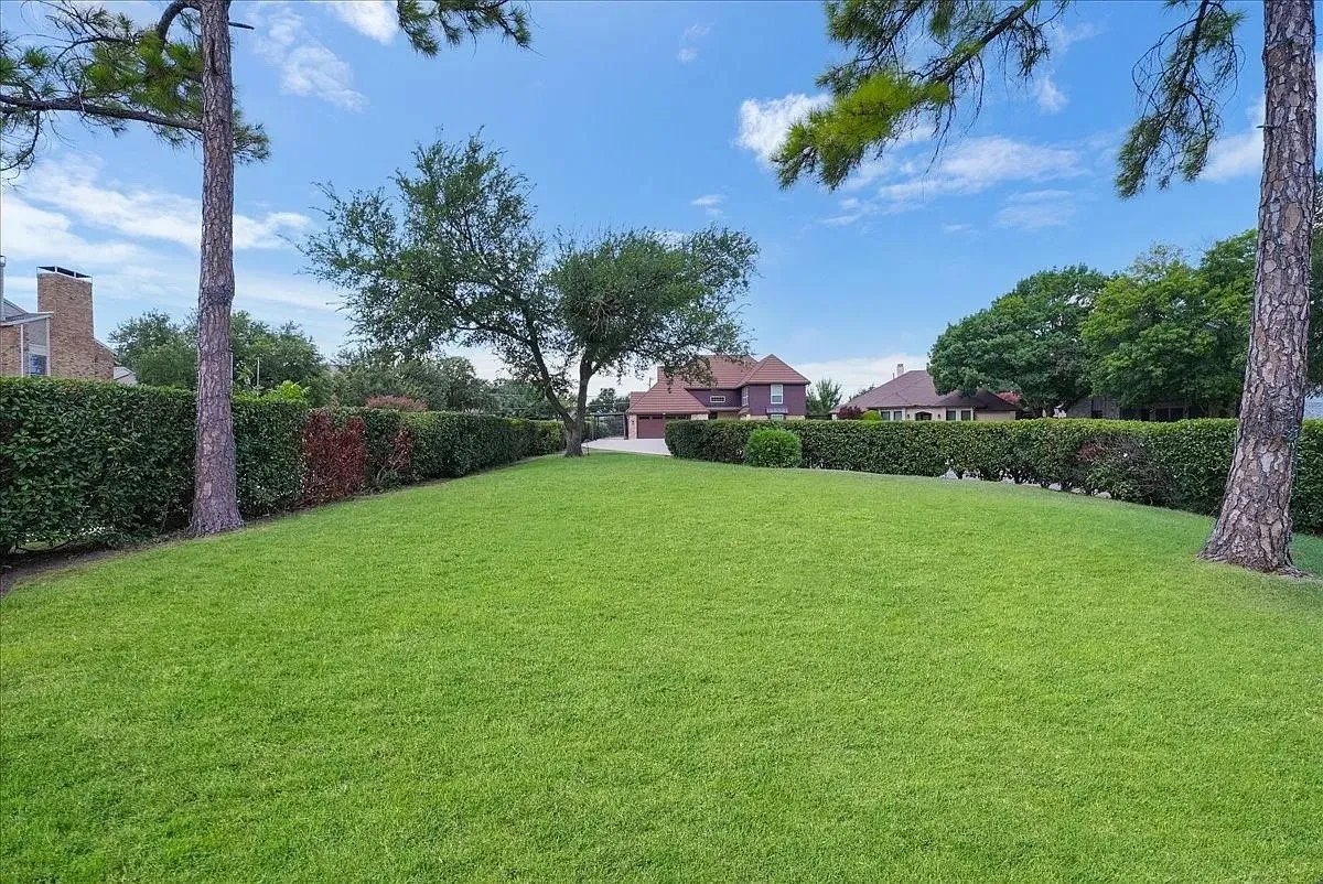 Expansive lawn area with mature trees and perimeter hedging