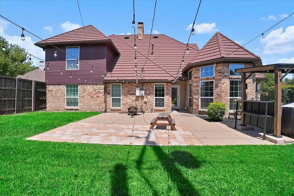 Expansive backyard featuring a paver patio with a concrete extension, a hot tub with a pergola, and a brick and siding exterior