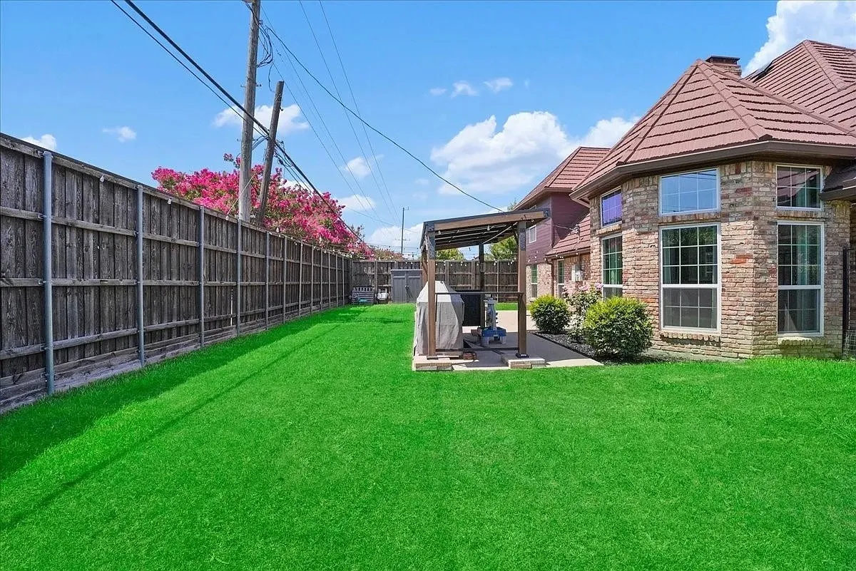 Expansive green lawn alongside a brick exterior with multiple windows, a brown tile roof, and a wood privacy fence