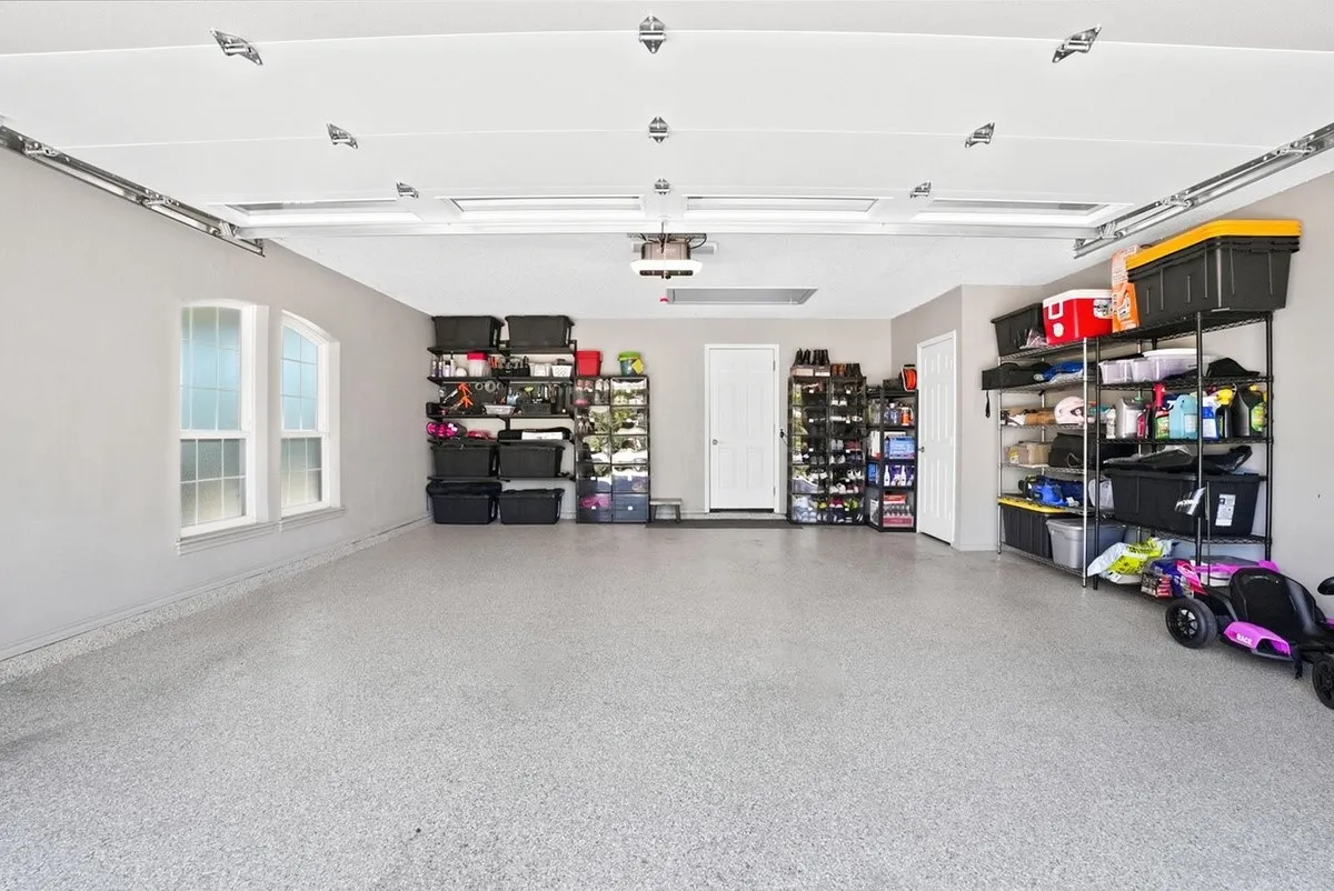 Spacious garage featuring a durable speckled epoxy floor, dual arched windows, flush-mounted ceiling lights, and multiple access doors