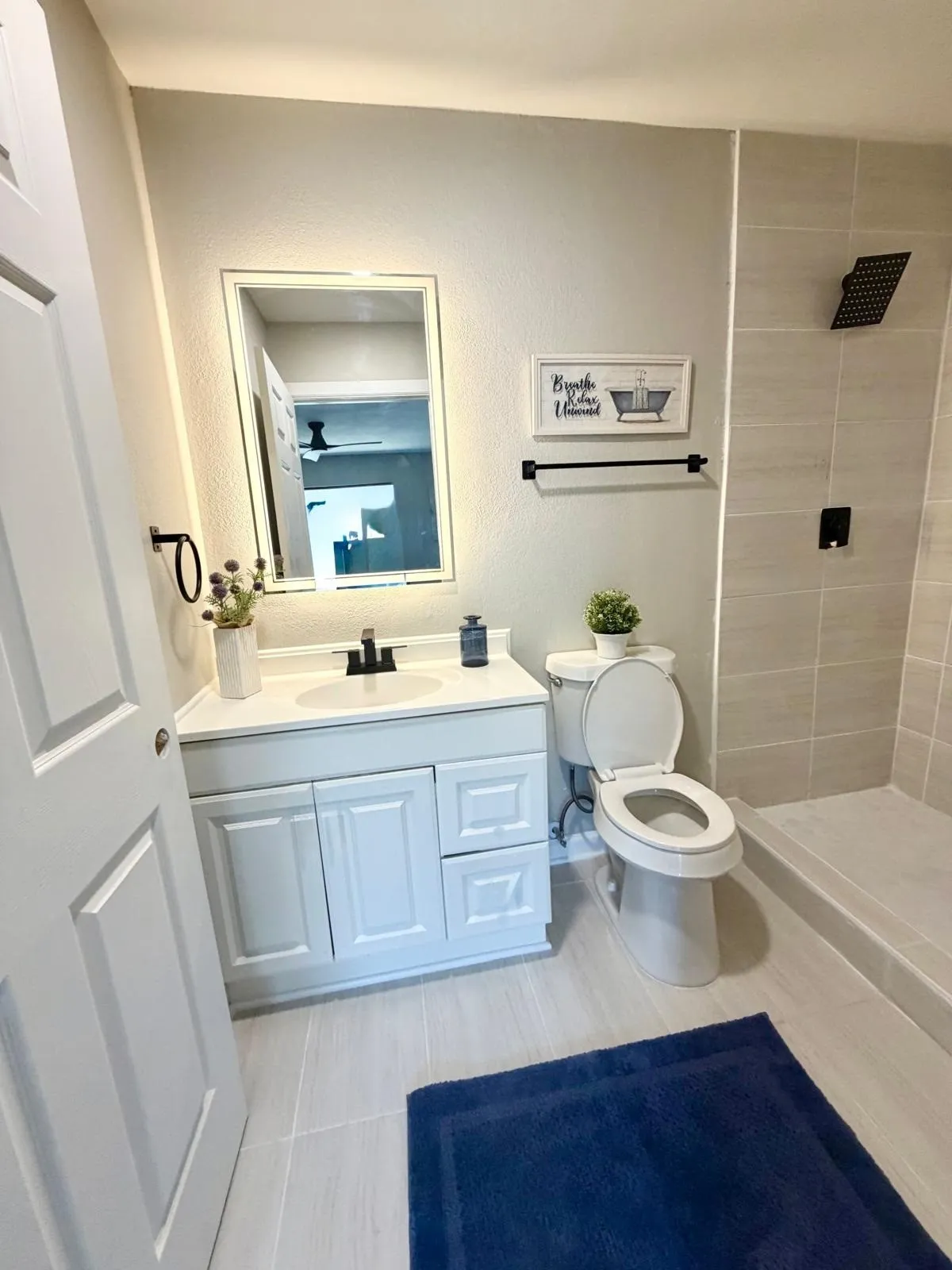 White vanity with integrated sink, matte black faucet, mirrored medicine cabinet, and tiled shower with rain shower head
