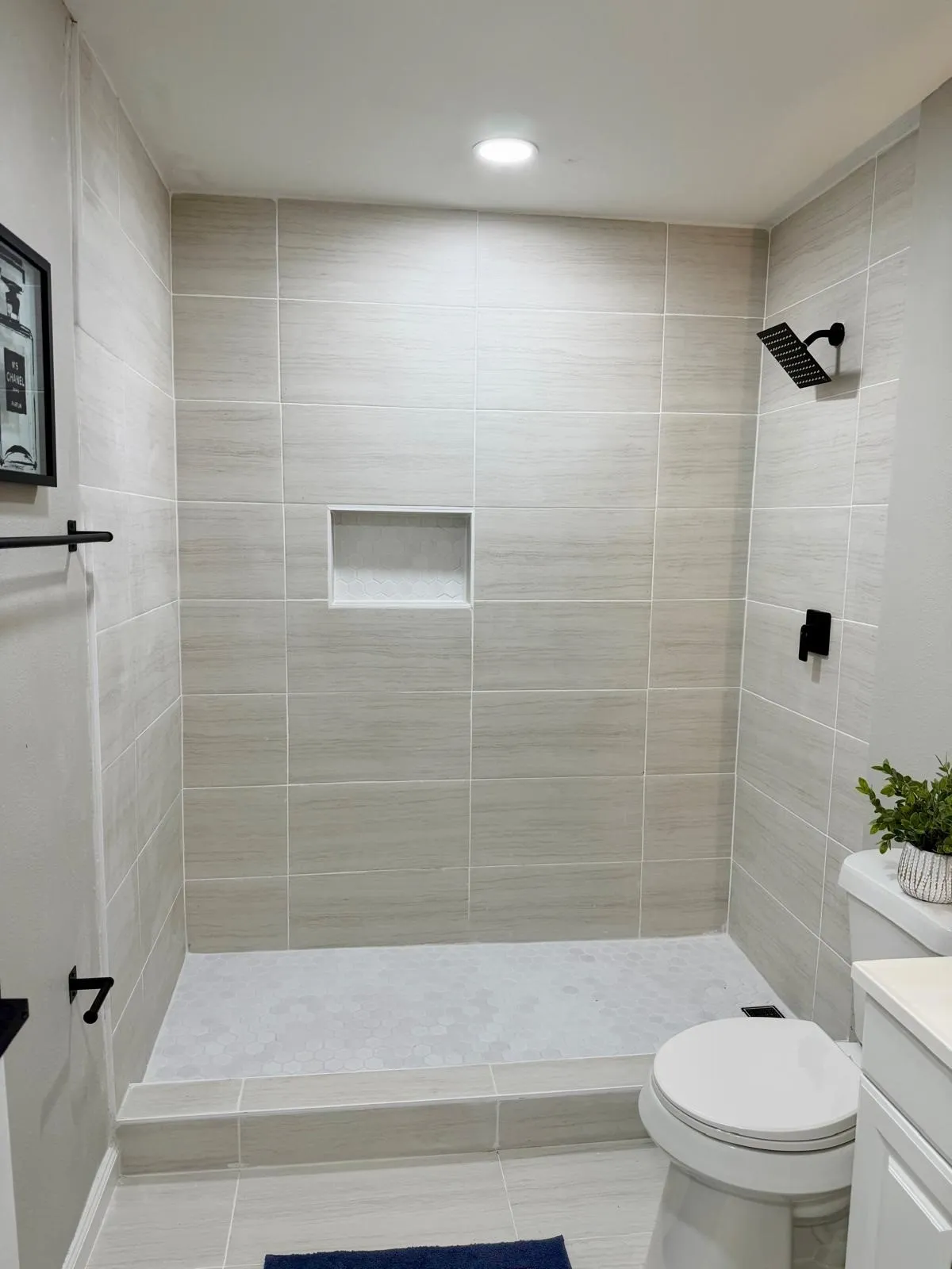 Tiled shower enclosure featuring a black matte rainfall showerhead, recessed shower niche, and tiled flooring