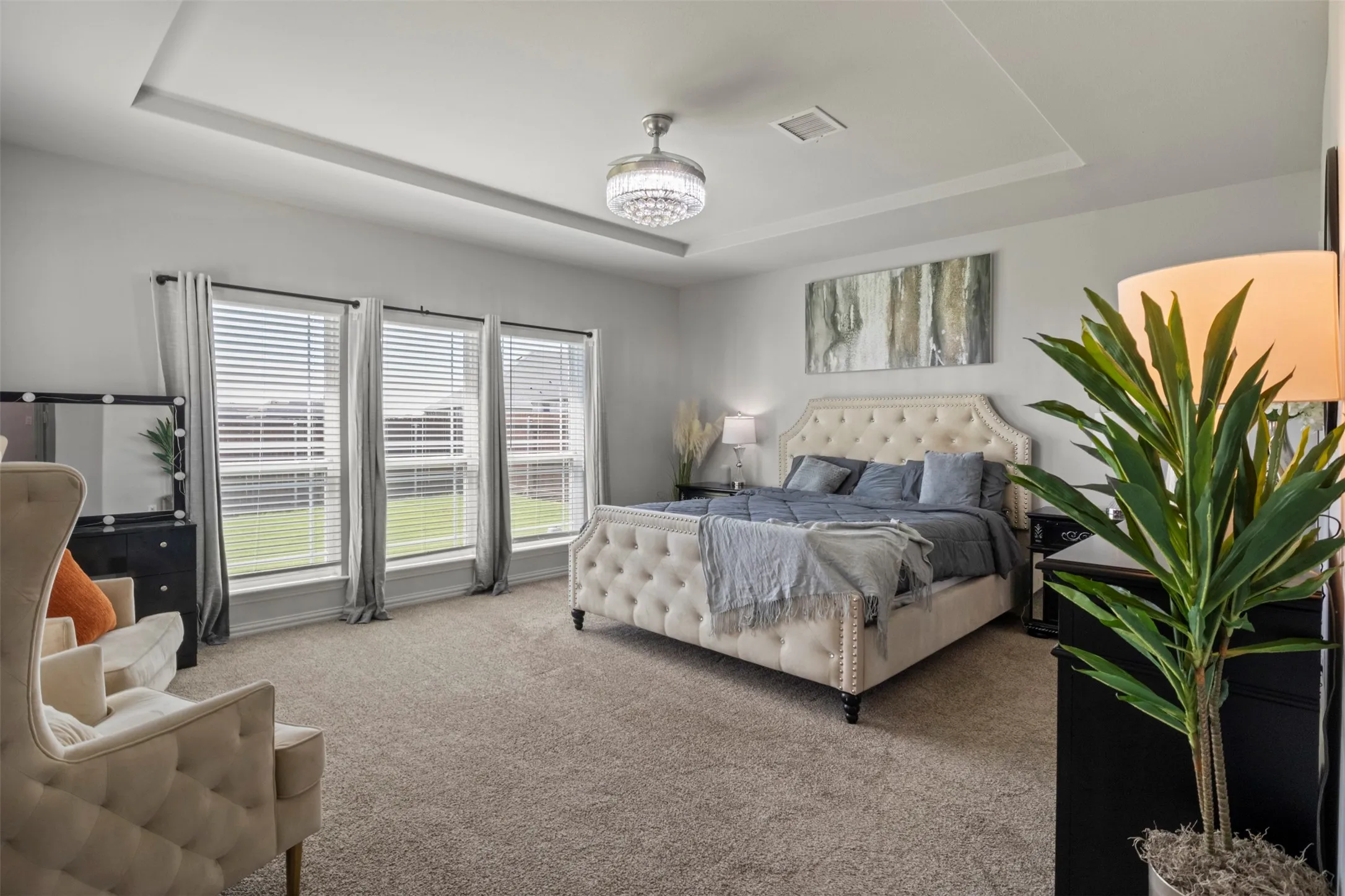 Tray ceiling with an embedded light fixture, light gray walls, large windows with blinds and curtains, and a neutral carpeted floor