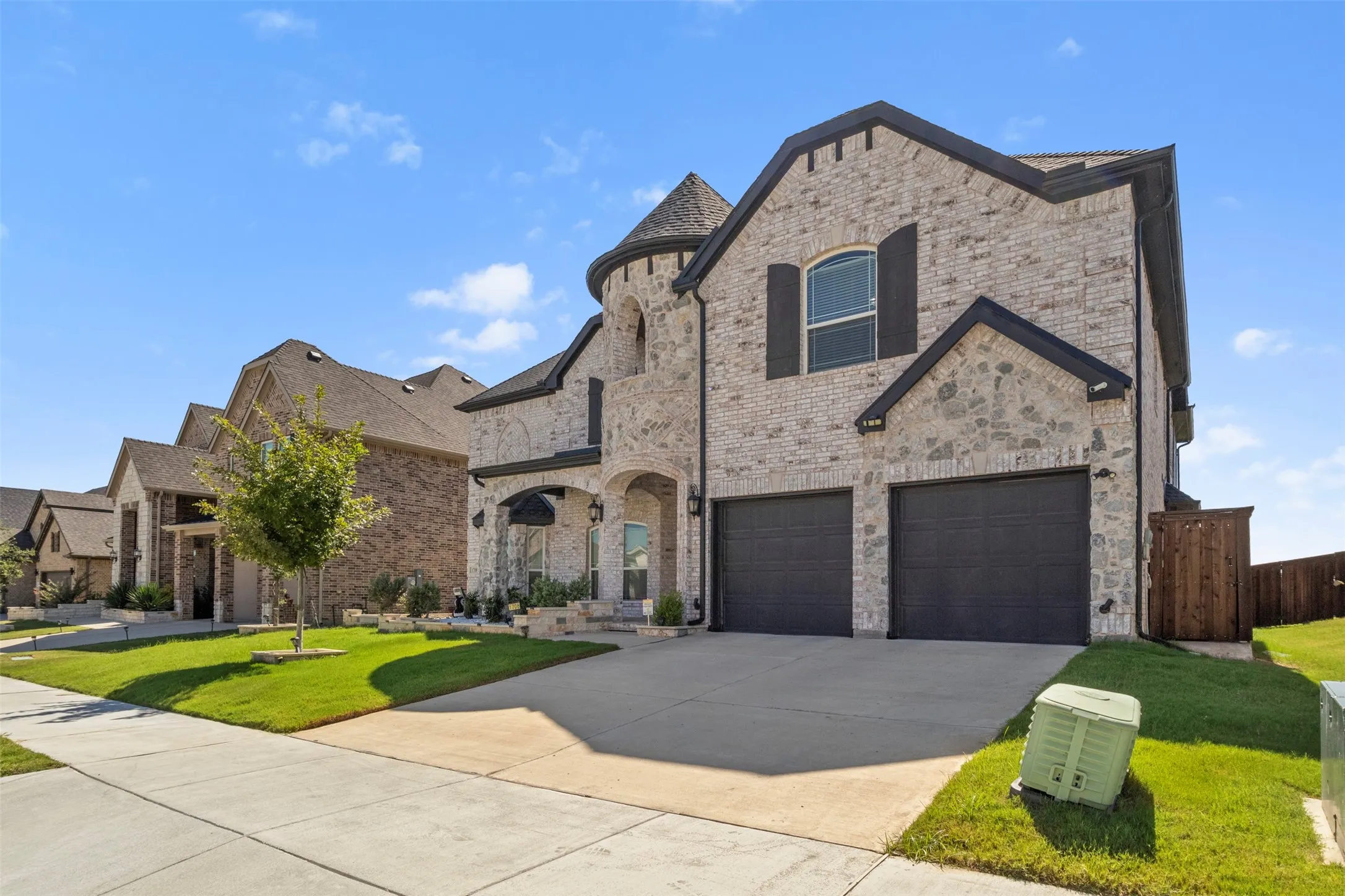 Stone and brick exterior with a turret feature, arched entry, two-car garage, and dark window shutters