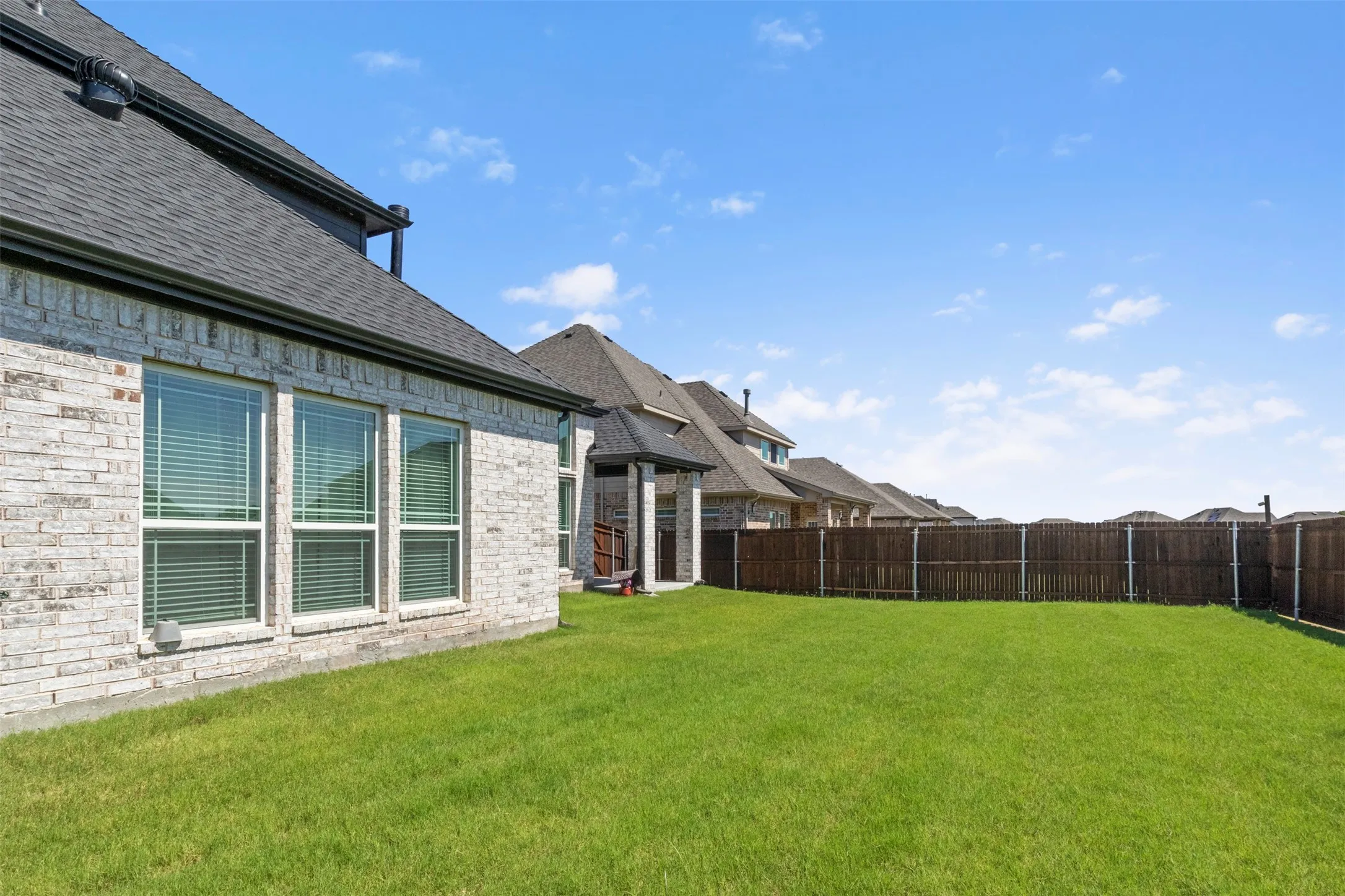 Expansive backyard featuring a lush lawn, privacy fencing, and a covered patio structure