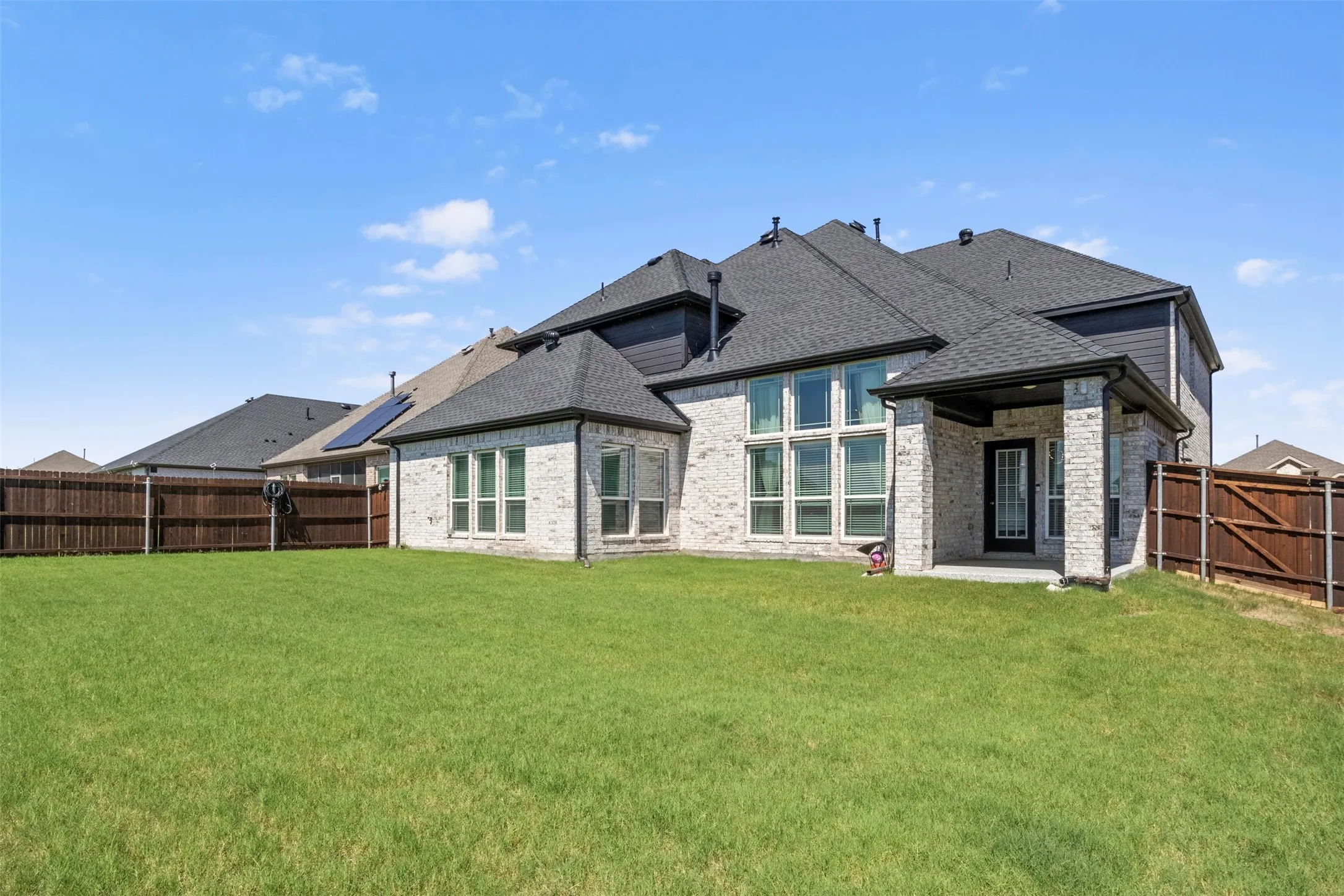Expansive backyard with a manicured lawn, full privacy fencing, and a covered patio