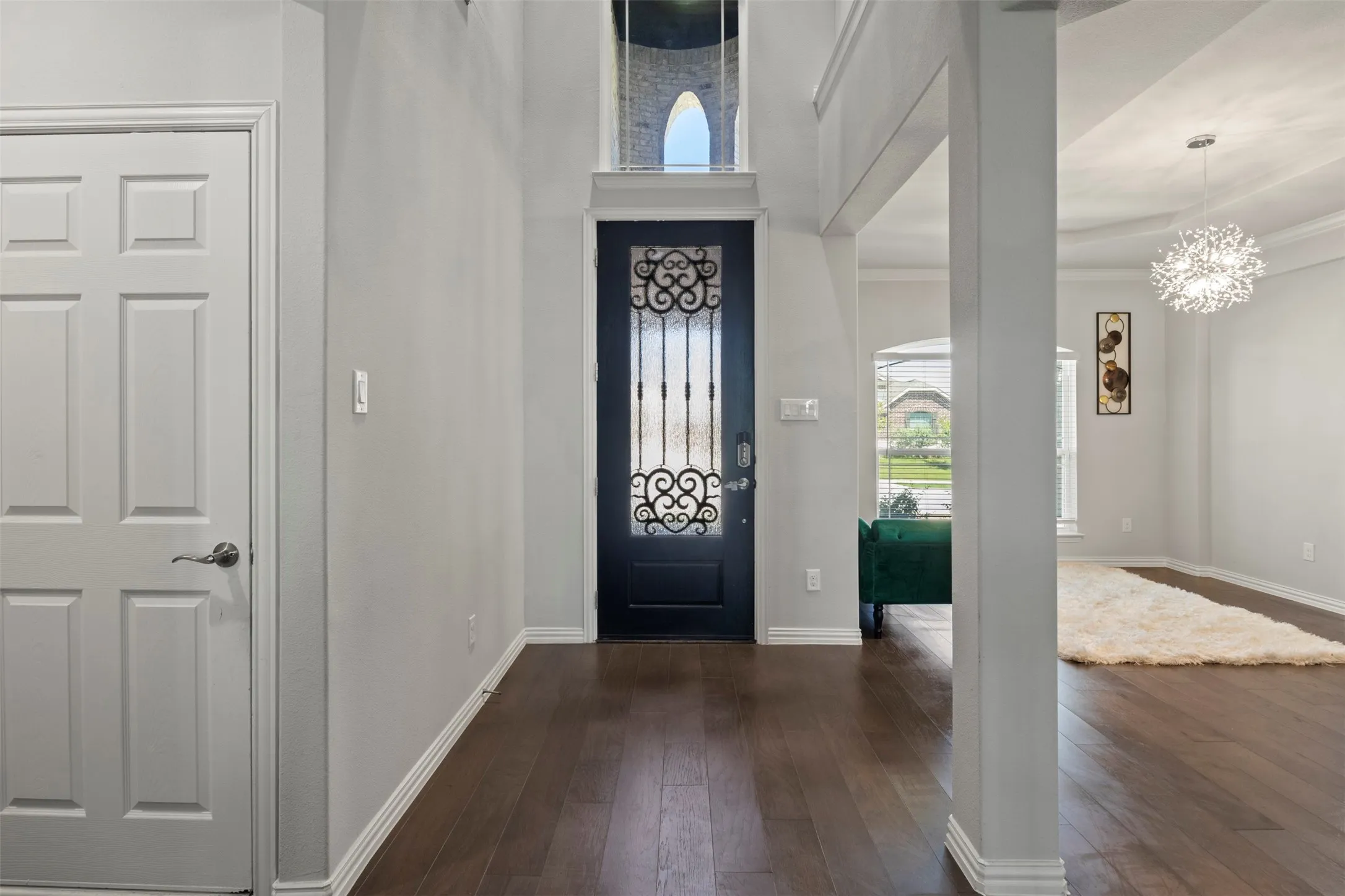 Double-height entryway featuring dark wood-finish flooring, a decorative glass-paneled entry door, and a modern spherical chandelier