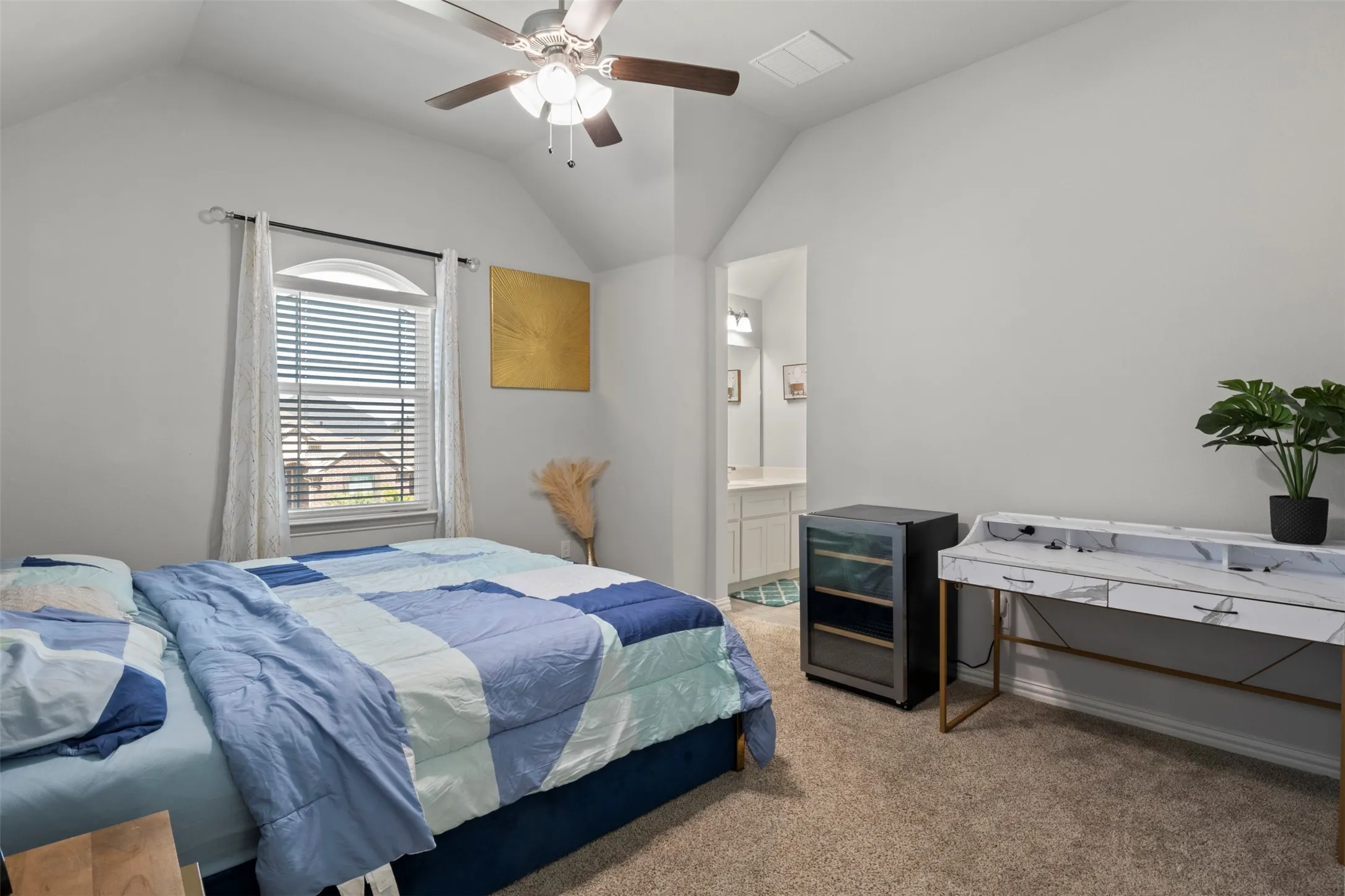 Vaulted ceiling, ceiling fan, arched window, carpet flooring, and an en-suite bathroom with a vanity featuring a vessel sink