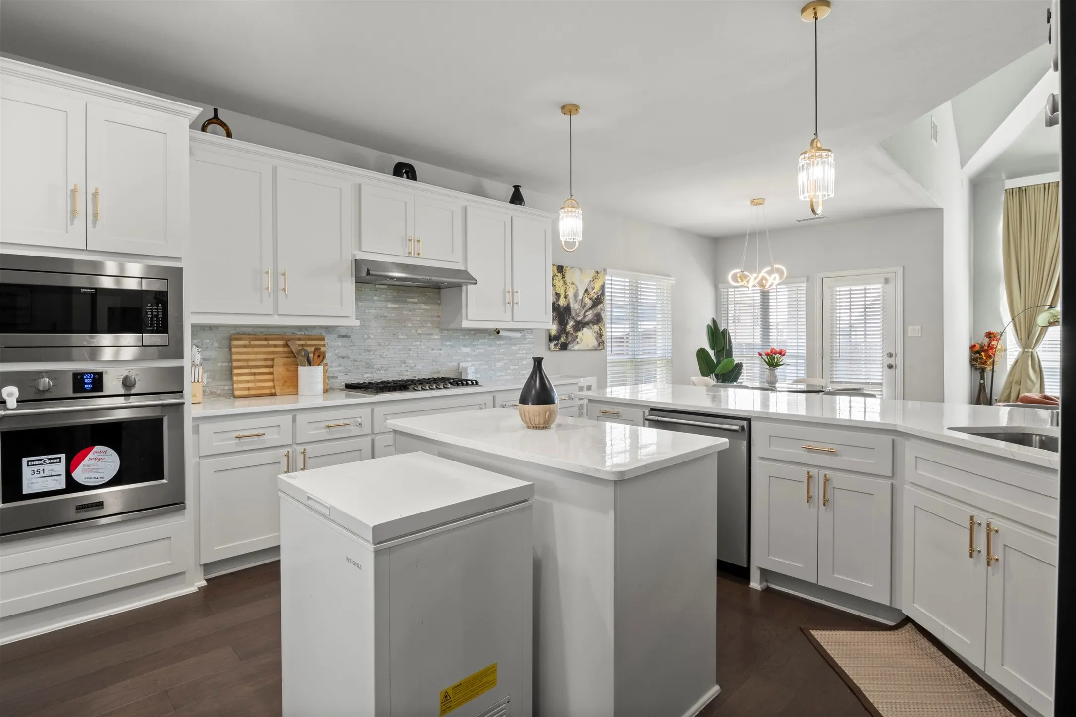White shaker cabinetry with gold-tone hardware, stainless steel appliances, light-toned backsplash, central island, and wood-finish flooring