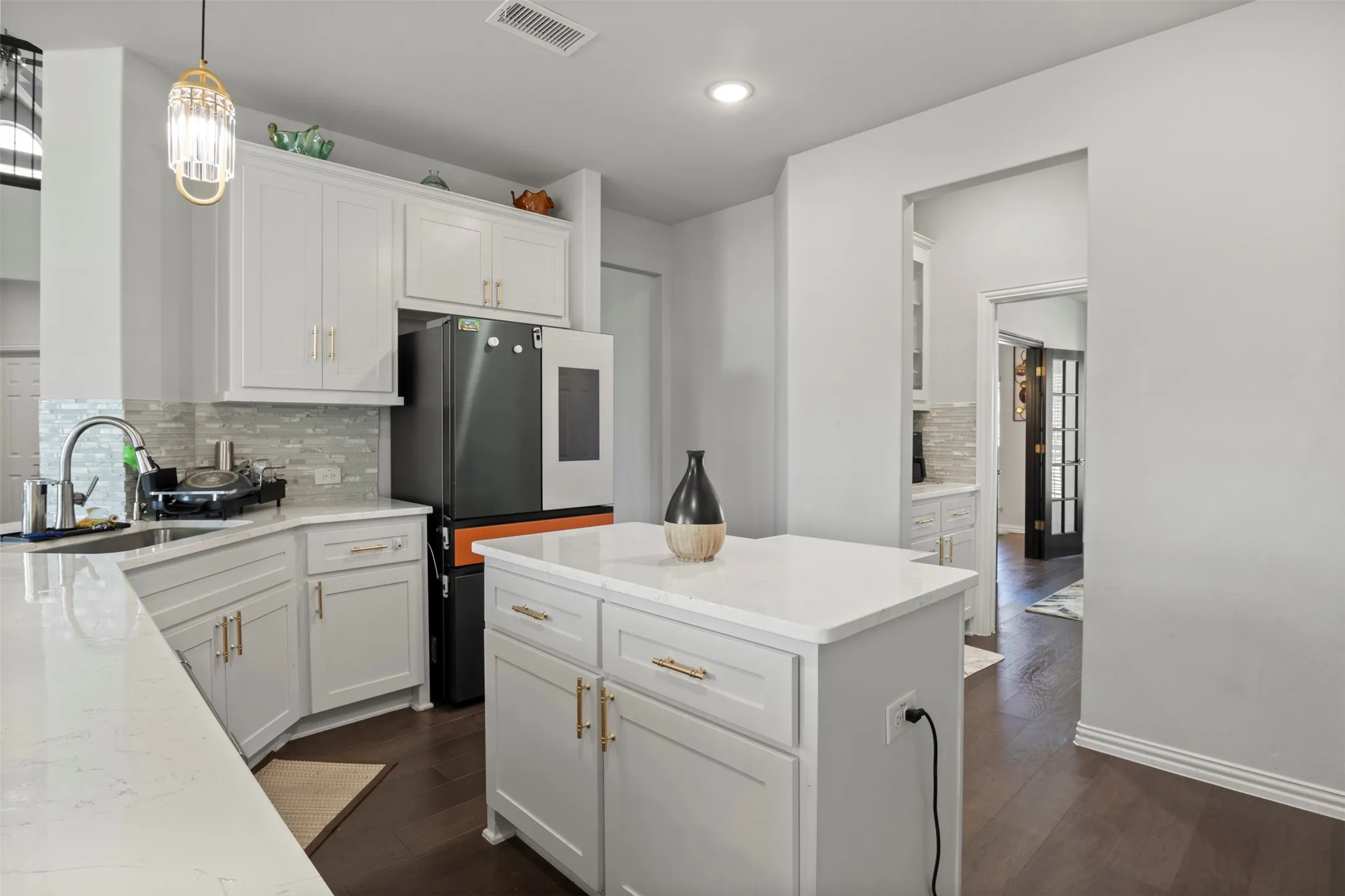 Kitchen featuring white shaker-style cabinetry, light-colored countertops, dark wood-finish flooring, a mosaic tile backsplash, and an island with built-in storage