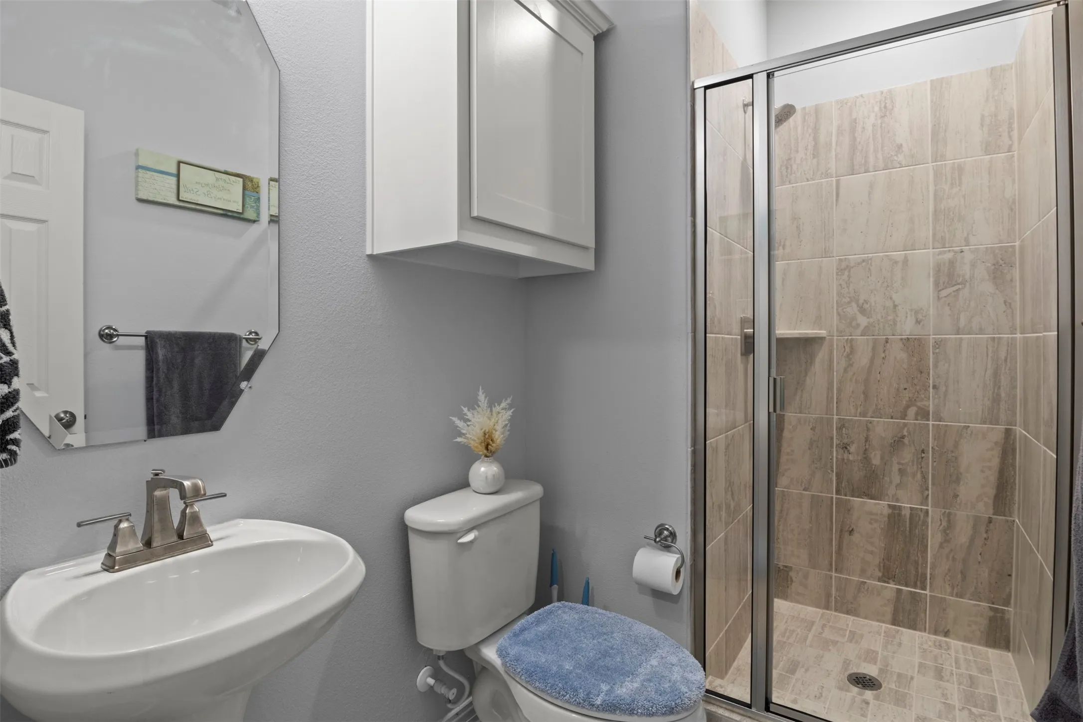 Pedestal sink, wall-mounted cabinetry, toilet, and tiled shower with glass enclosure