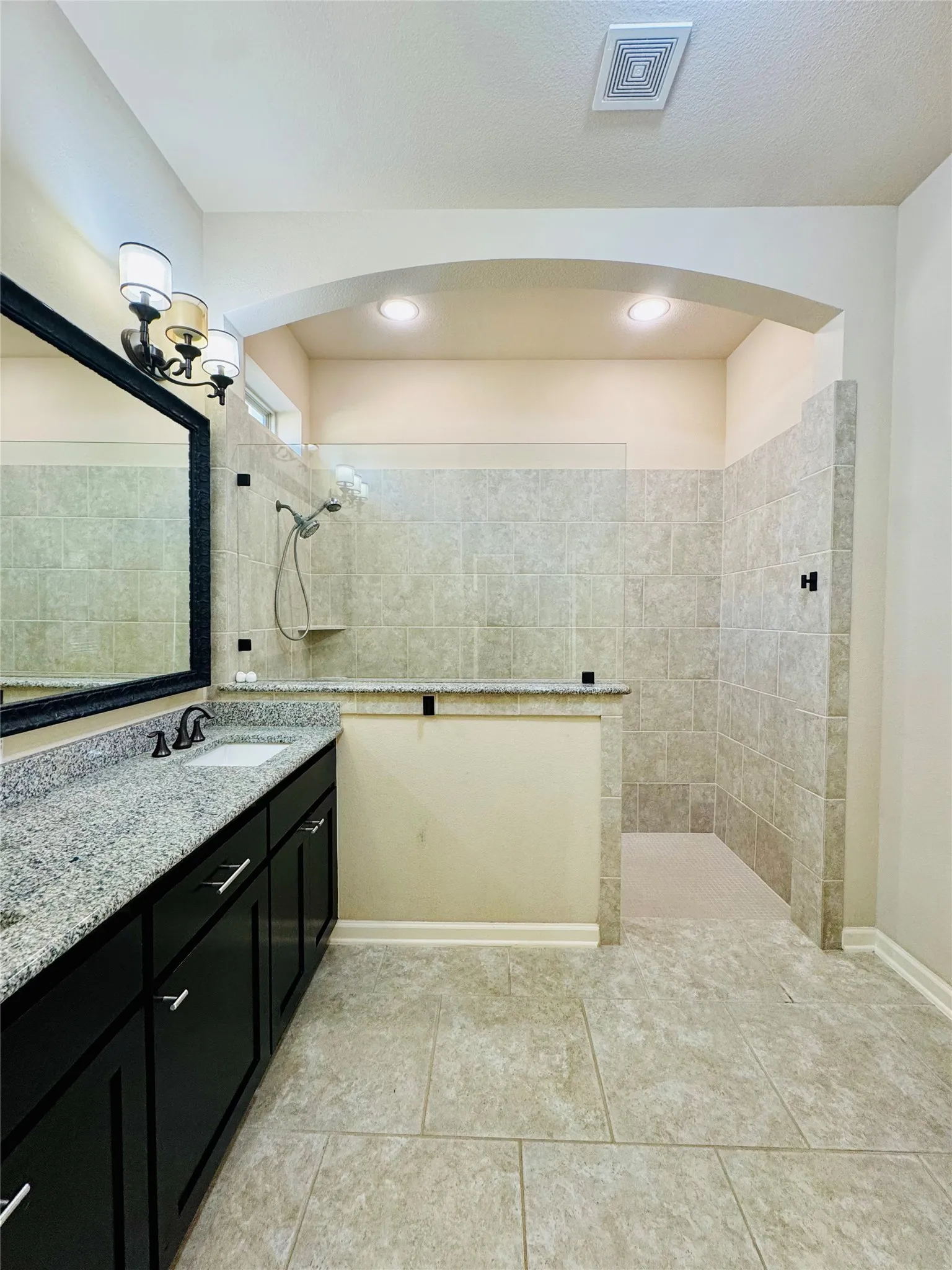 Spacious bathroom featuring a walk-in shower with full wall tiling, a vanity with a granite-style countertop, and tile flooring
