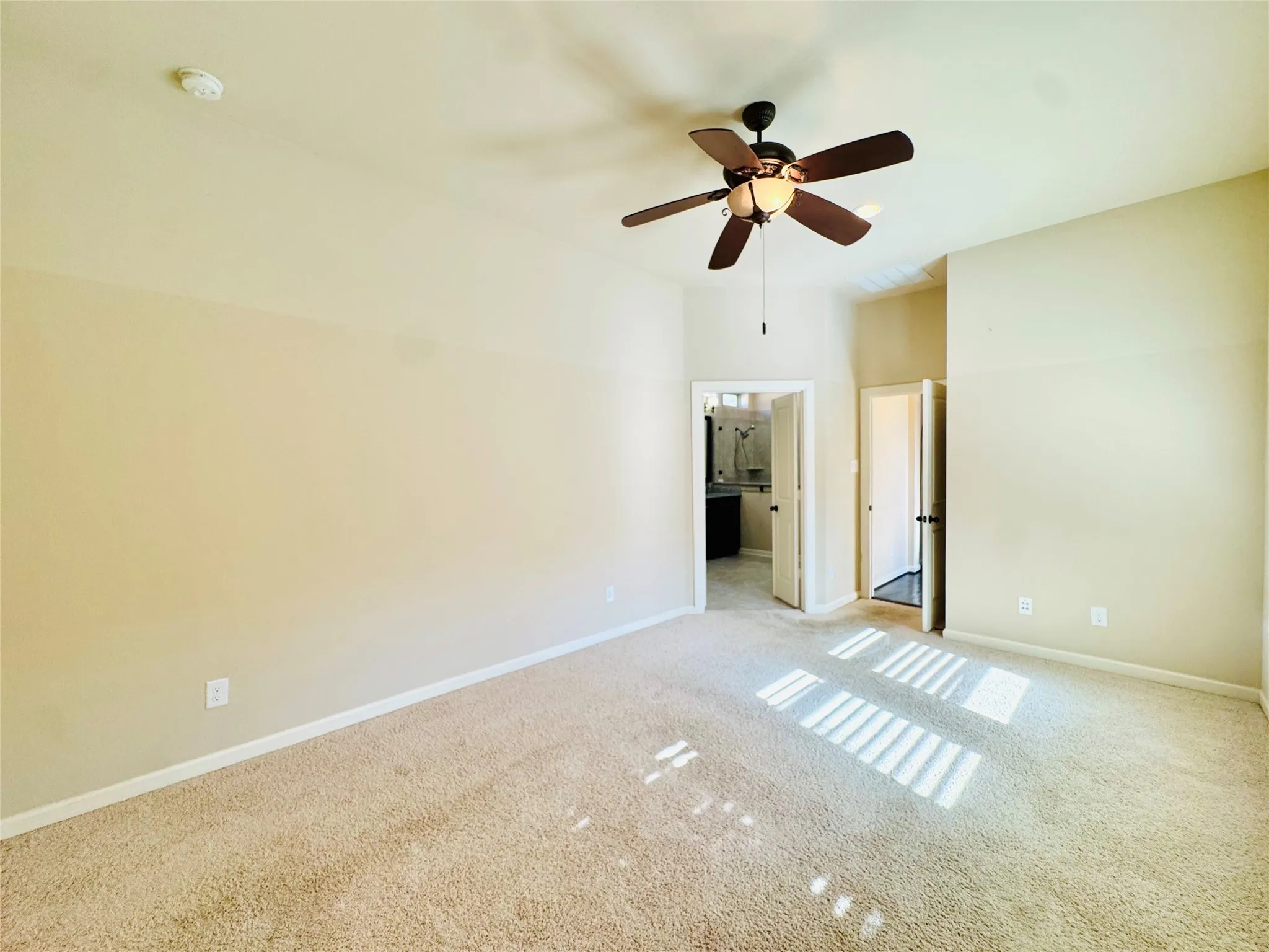Neutral wall paint, carpet flooring, a ceiling fan with light, and an open doorway