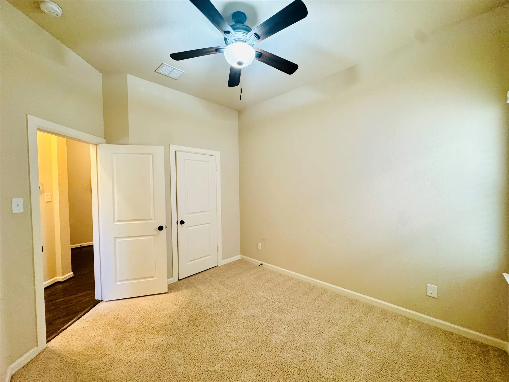 Neutral-toned wall paint, carpet flooring, a ceiling fan with integrated lighting, and white paneled doors with black hardware