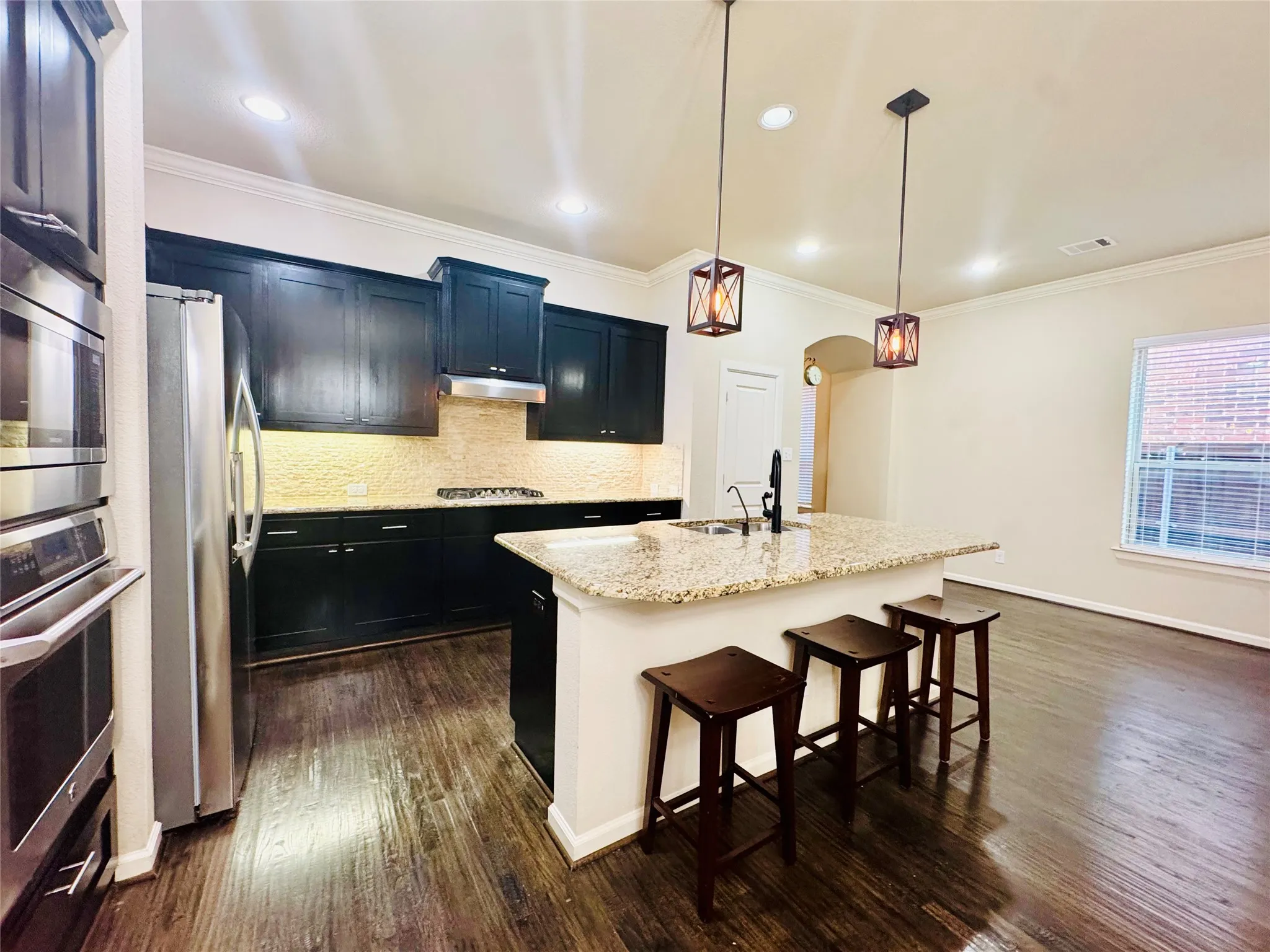 Kitchen featuring dark wood-finish cabinetry, stainless steel appliances, a textured tile backsplash, an island with a granite countertop, and recessed lighting