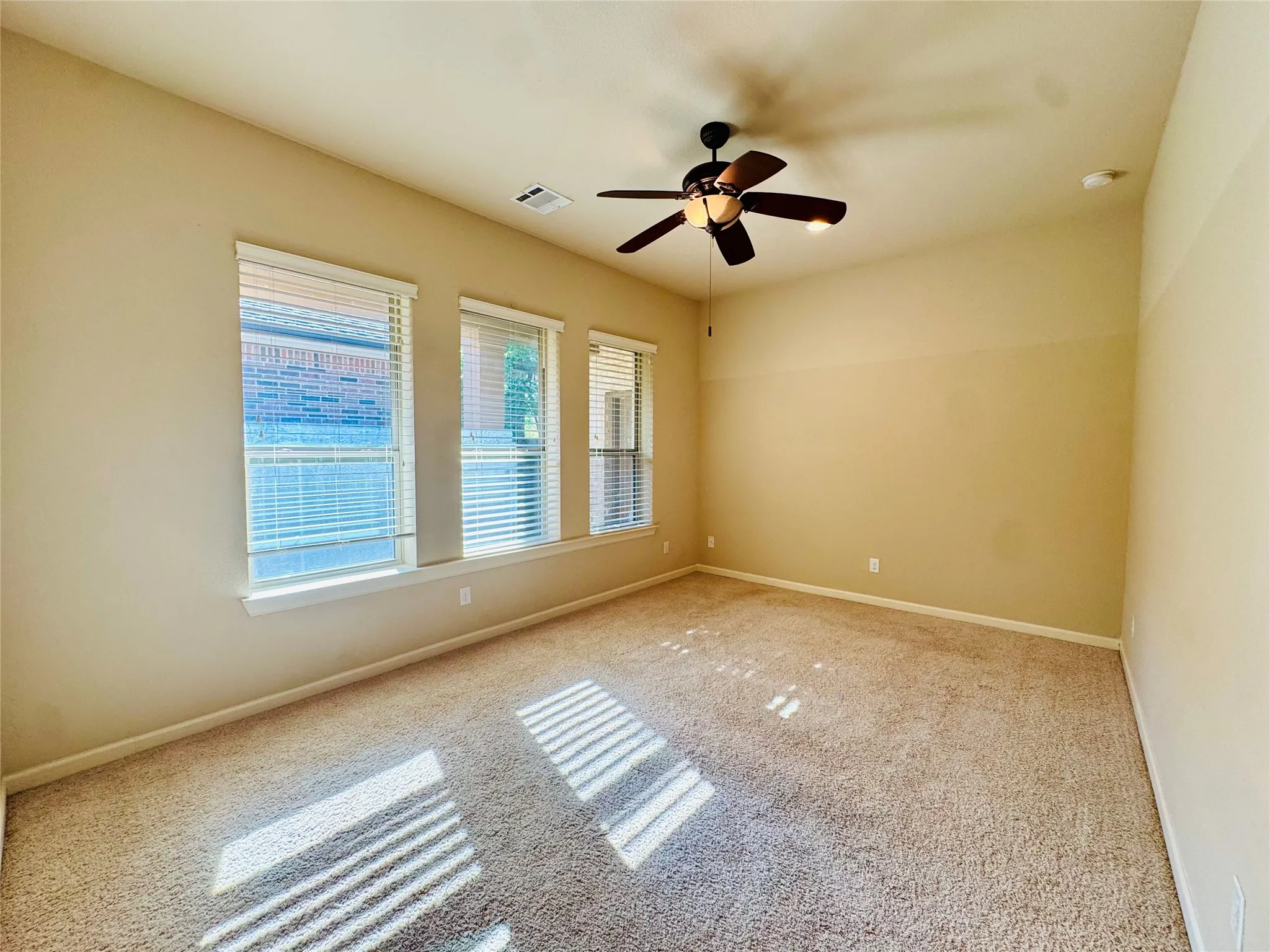 Carpeted room with a ceiling fan, multiple windows with blinds, and neutral-toned walls