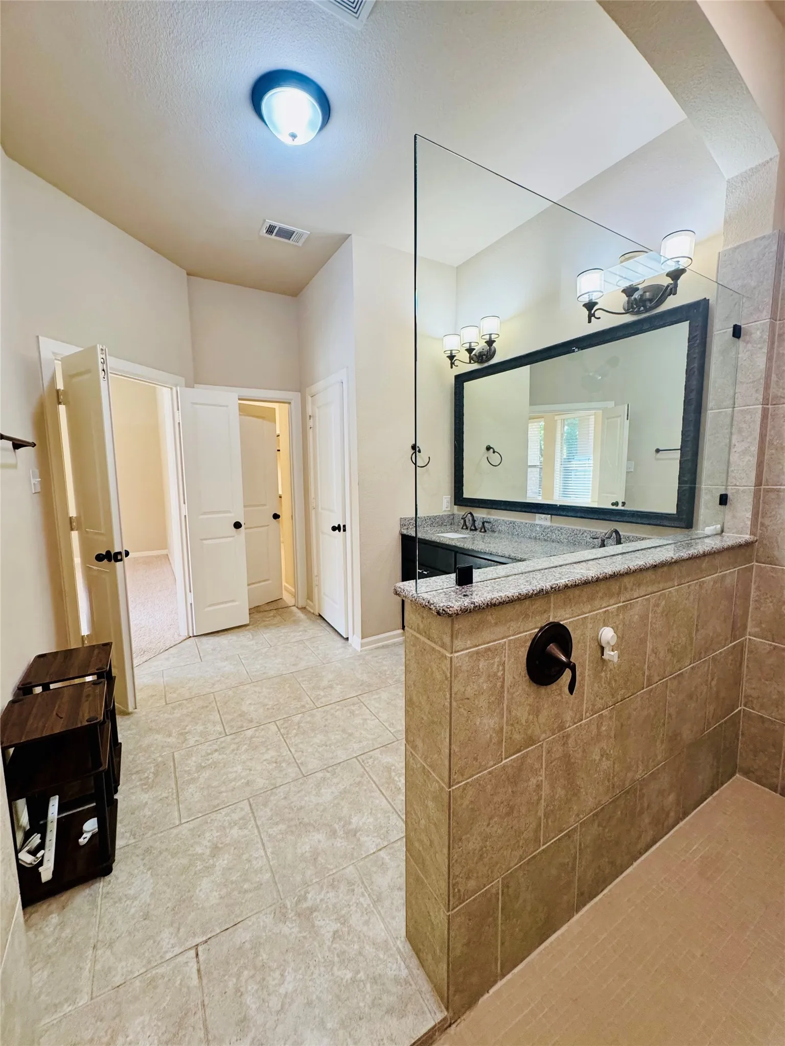 Spacious bathroom featuring a dual vanity with granite countertop, large rectangular mirror, and tiled walk-in shower with a glass partition