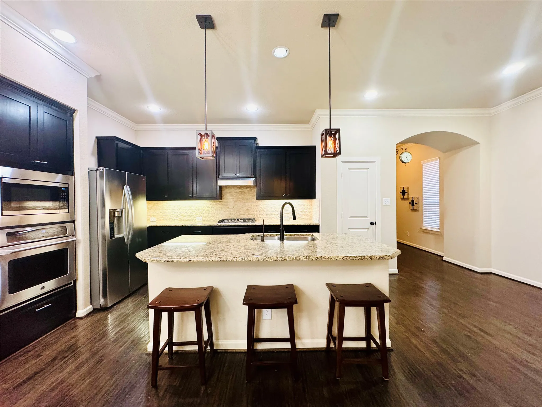 Kitchen featuring dark wood-finish cabinetry, stainless steel appliances, a center island with a light-toned countertop, a tile backsplash, and dark wood-finish flooring